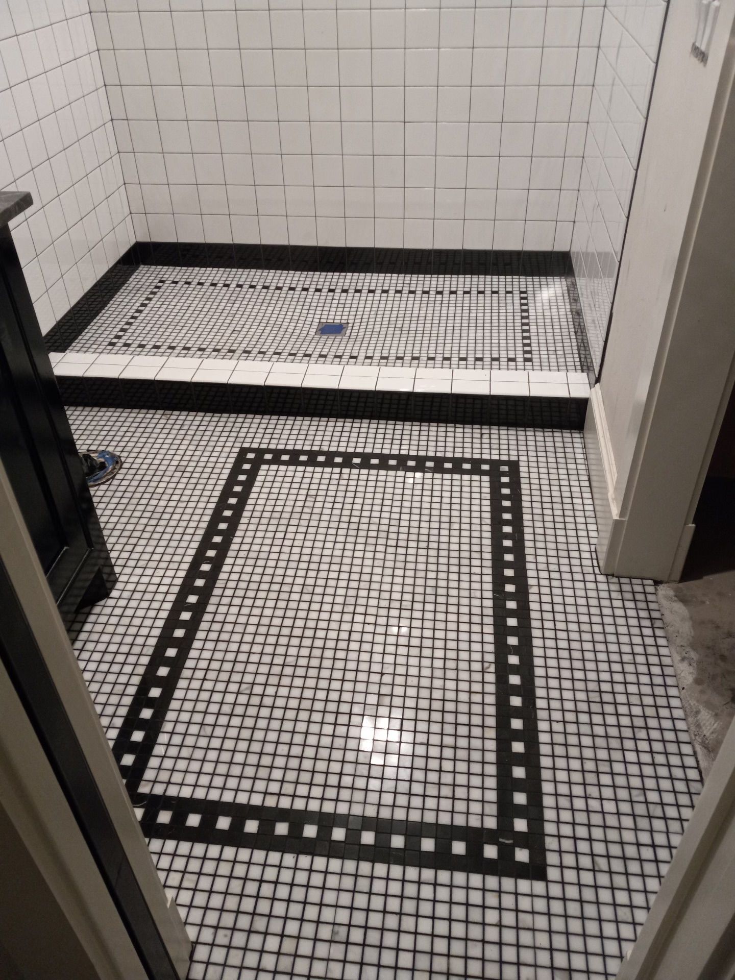 A bathroom with a black and white tile floor and a shower stall.