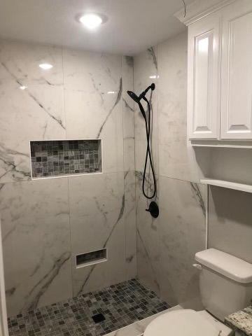 A bathroom with a walk in shower , toilet , and cabinets.