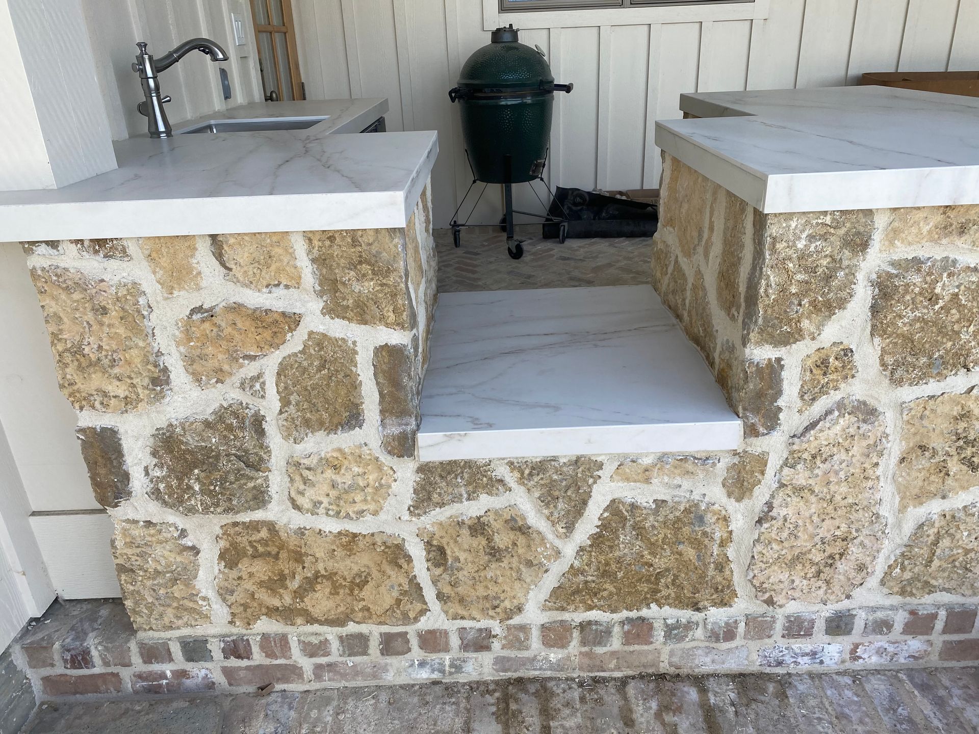 A stone wall with a sink and a grill in the background.
