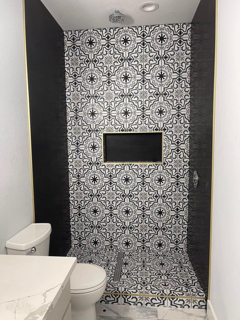 A bathroom with a toilet and a shower with a black and white tile wall.