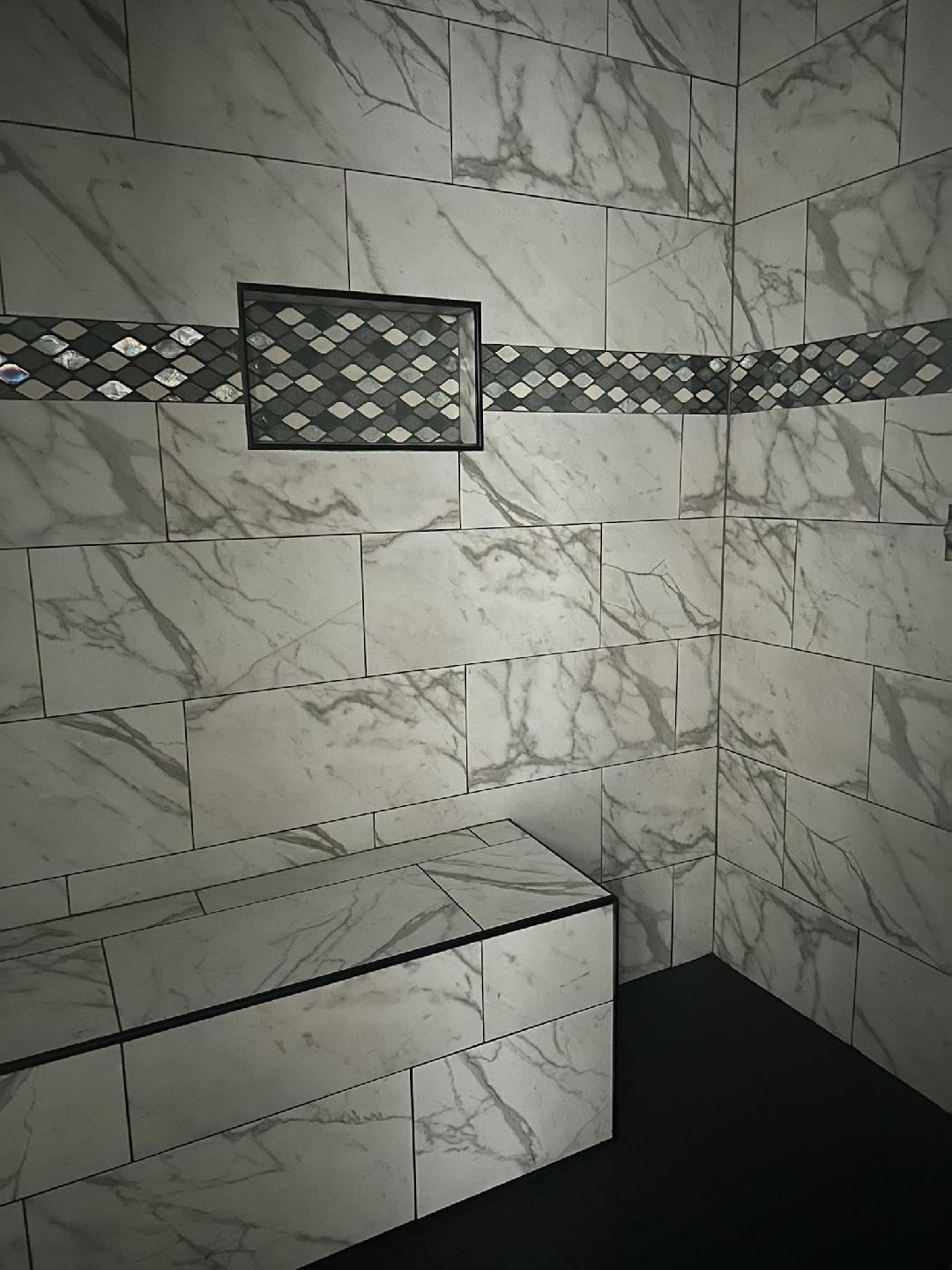 A bathroom with marble tiles and a bench in the shower.