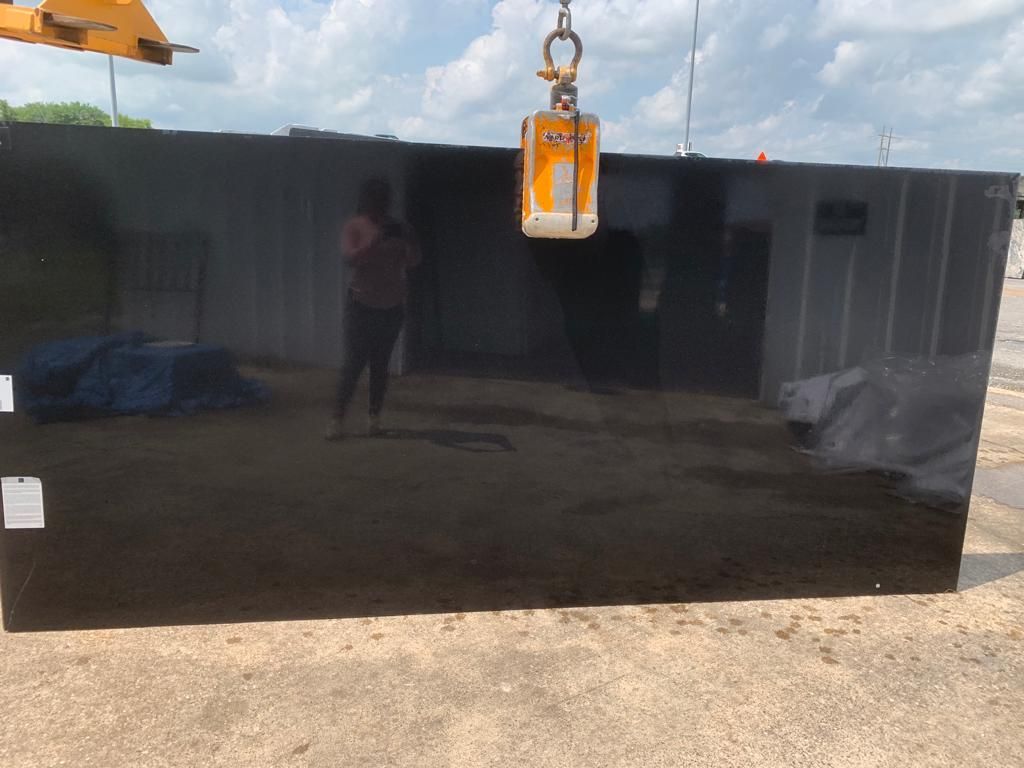 A large black granite slab is being lifted by a crane.