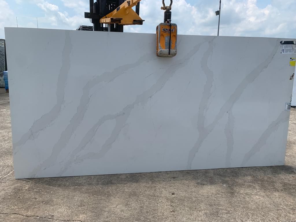 A large white slab of granite is being lifted by a crane.
