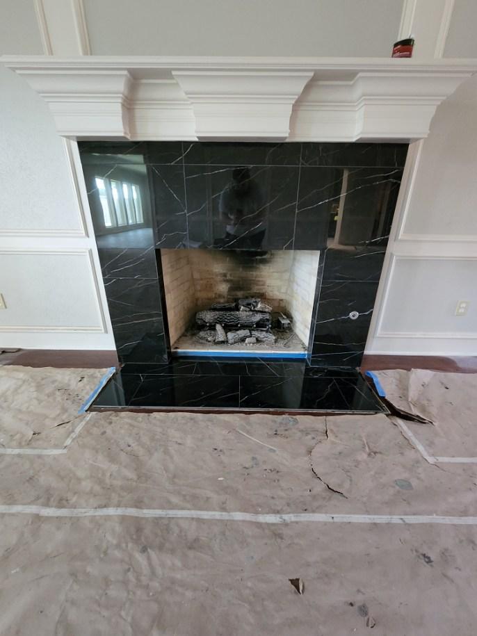 A fireplace in a living room with black tiles and a mantle.