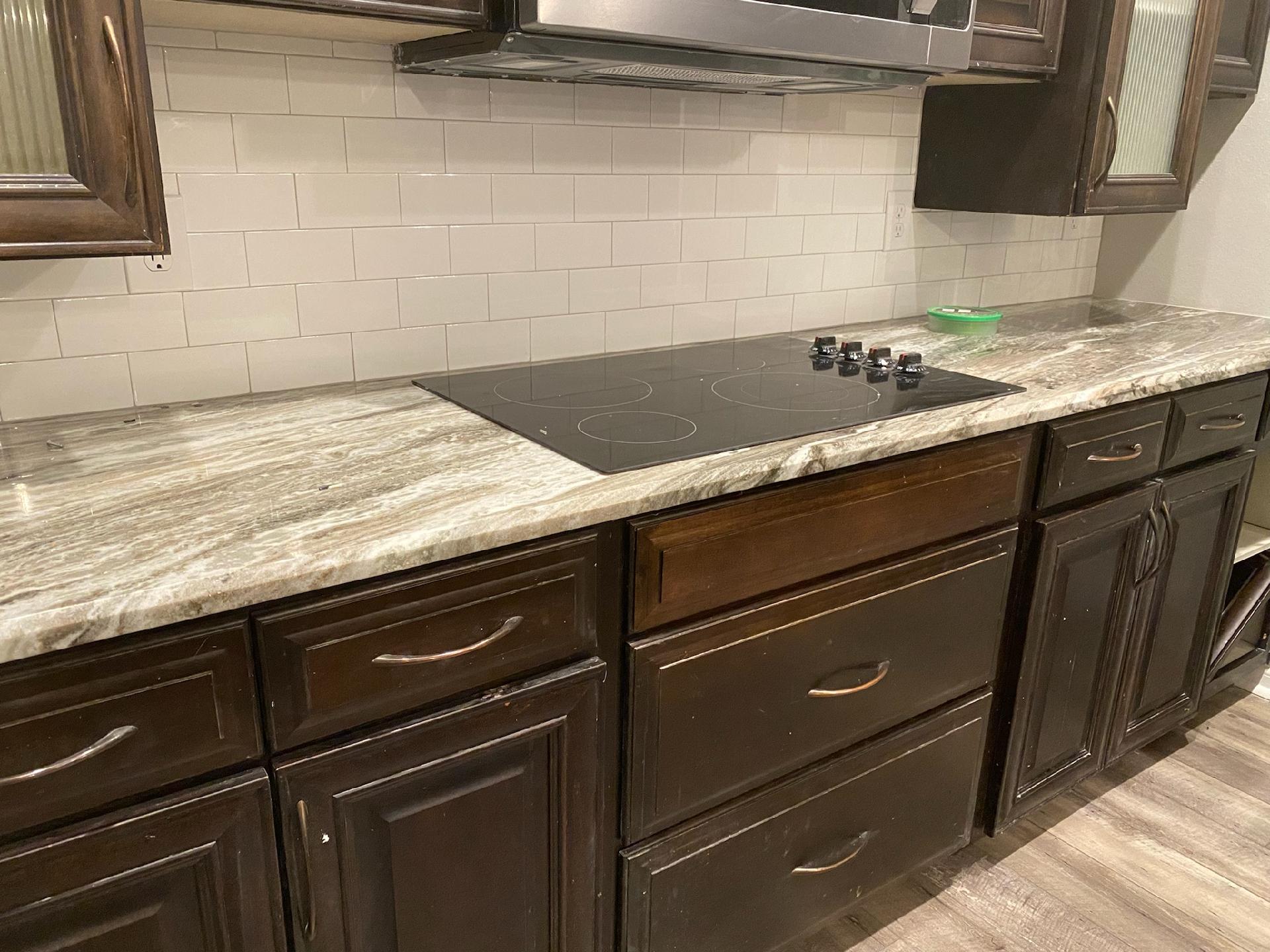 A kitchen with wooden cabinets , granite counter tops , and a stove top oven.