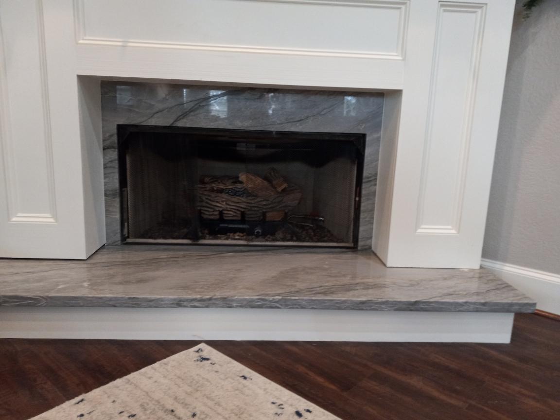 A fireplace with a marble mantle and a wooden floor in a living room.