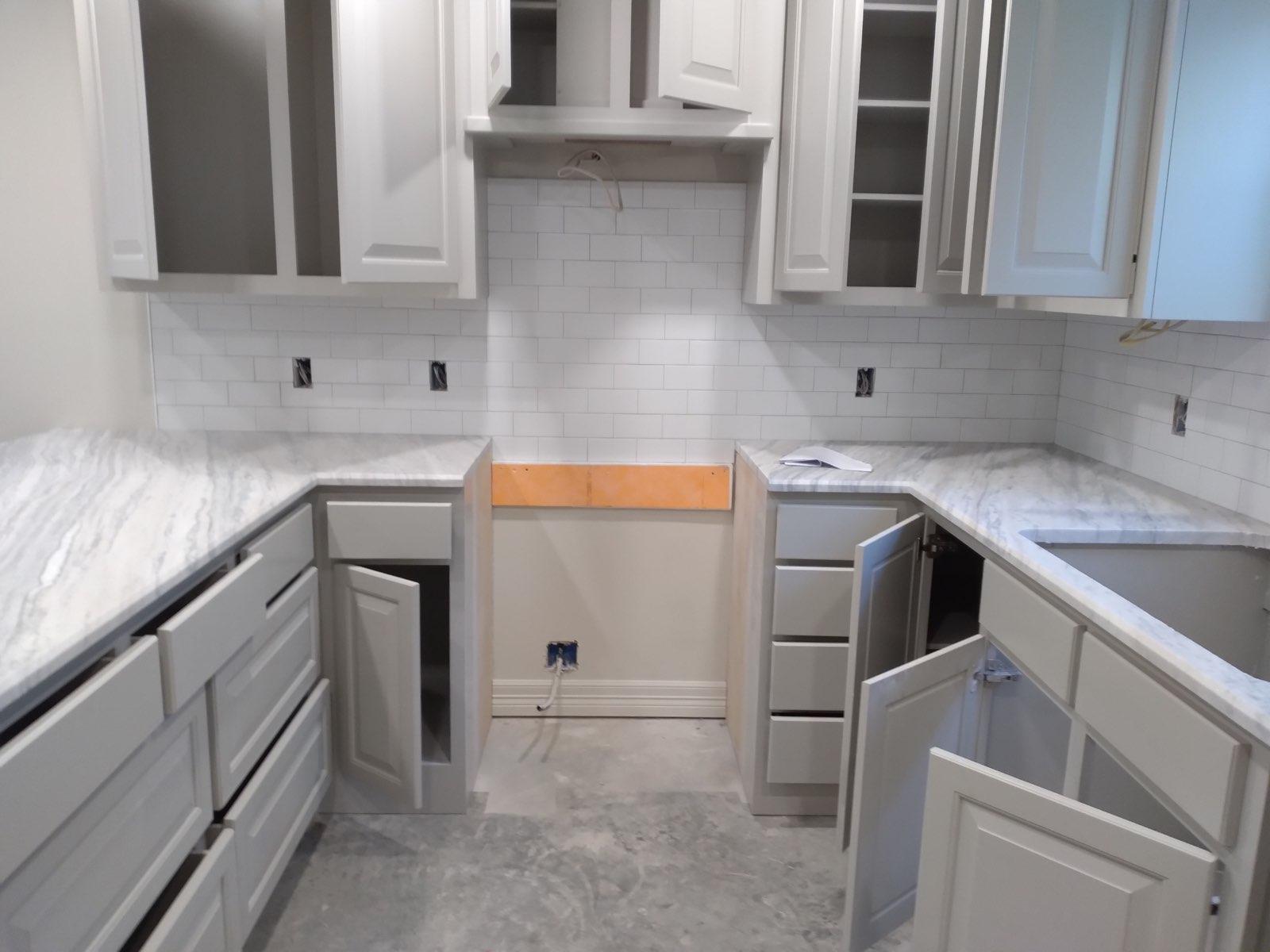 A kitchen with white cabinets and marble counter tops