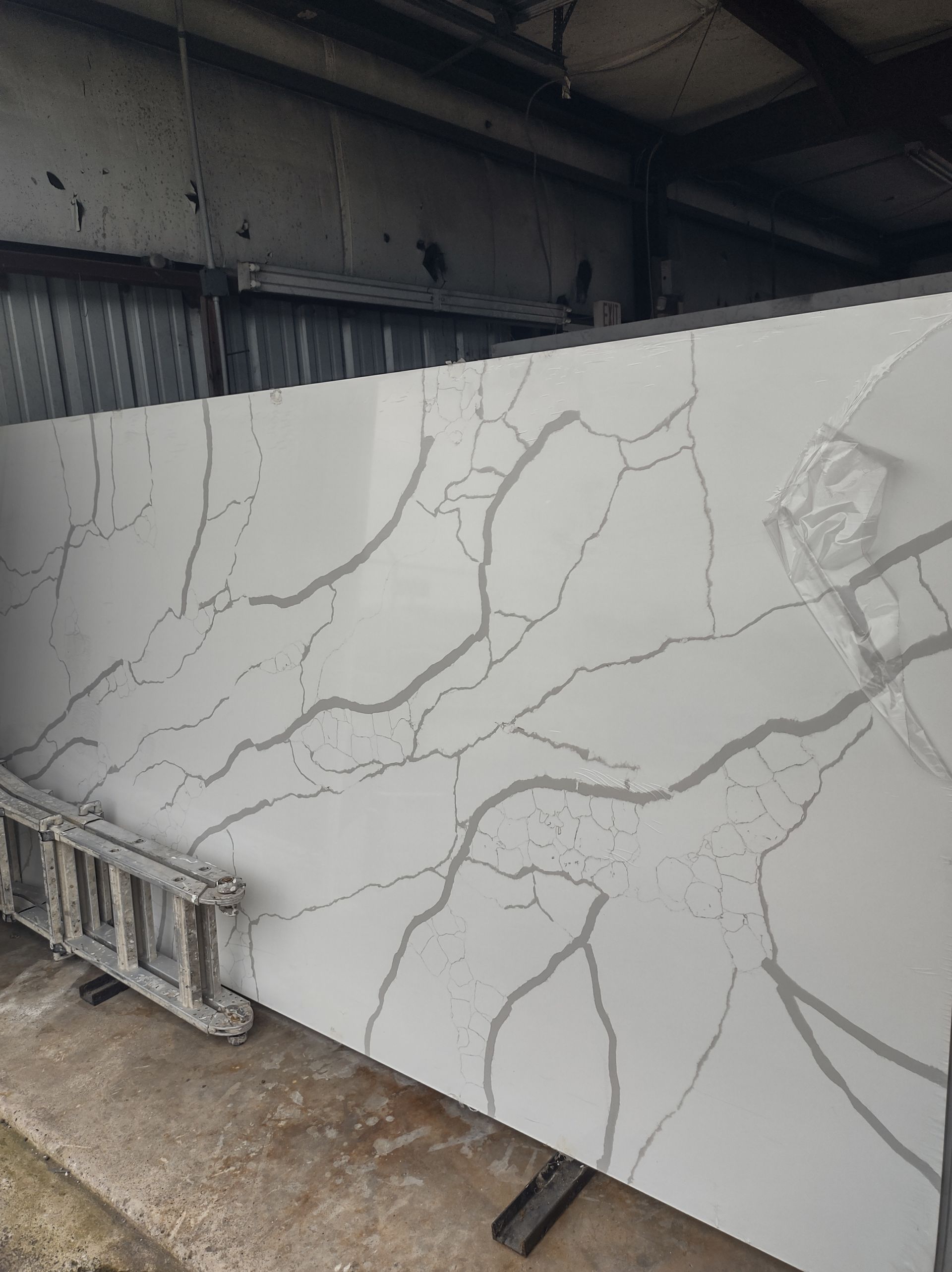 A large white granite slab is sitting on the ground next to a ladder.