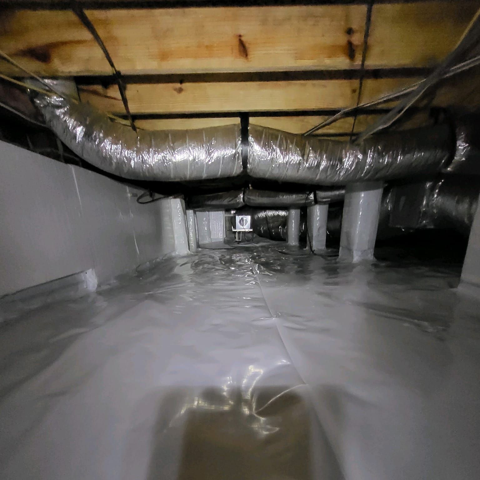 A crawl space with a lot of pipes and ducts in it.