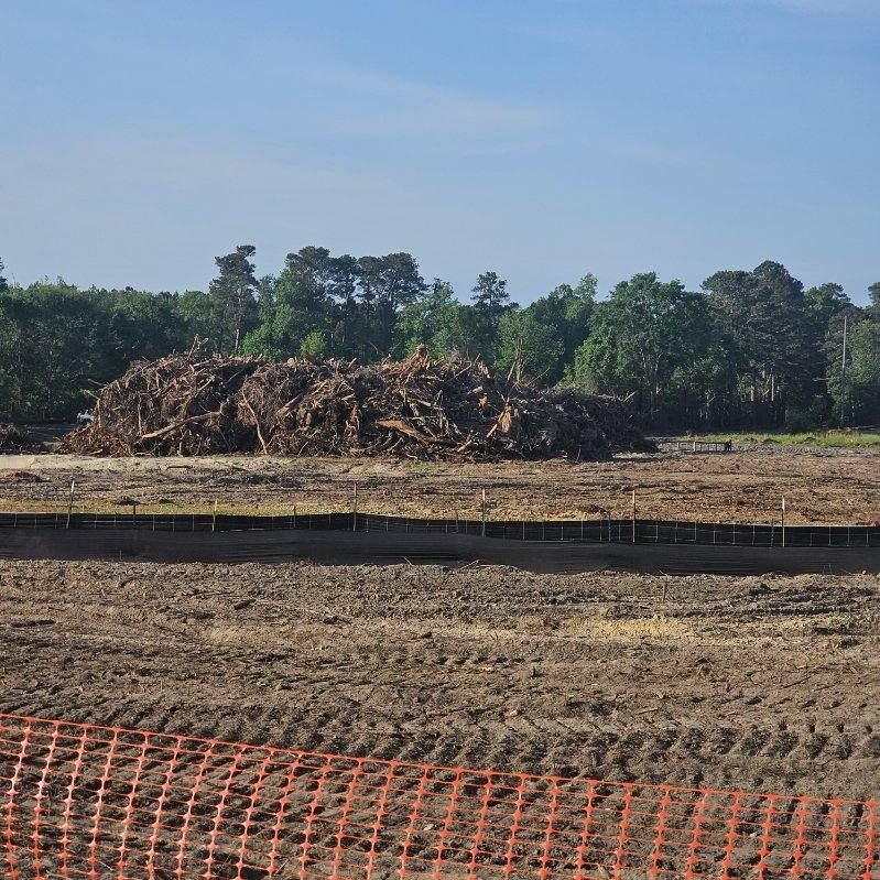 A large pile of logs is in the middle of a dirt field
