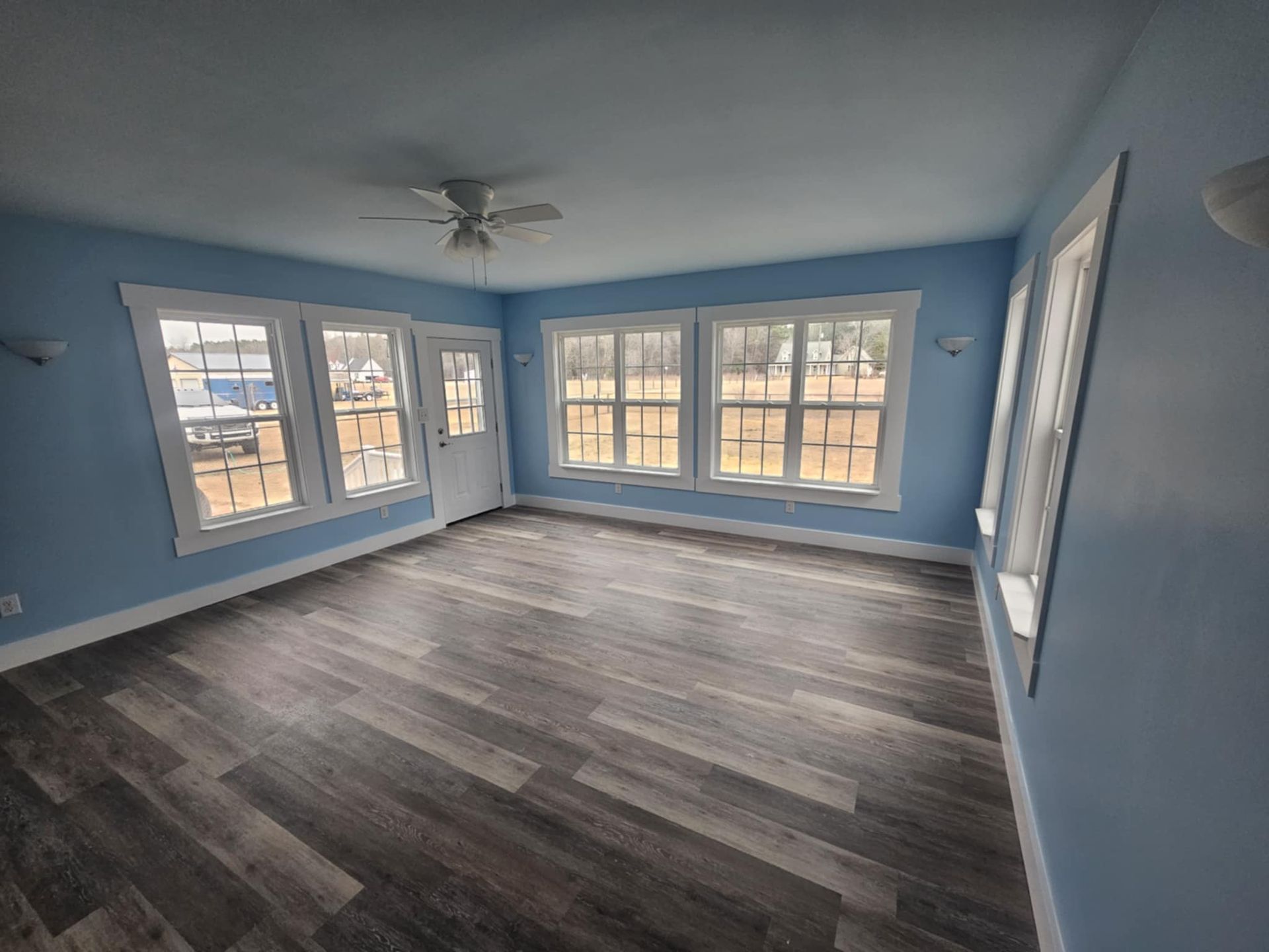 An empty living room with blue walls and a ceiling fan.