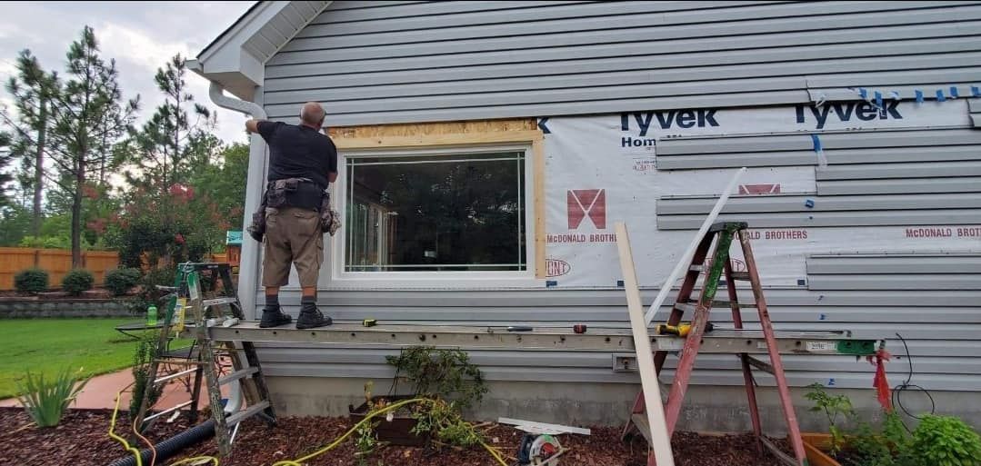 A man is installing a window on the side of a house.