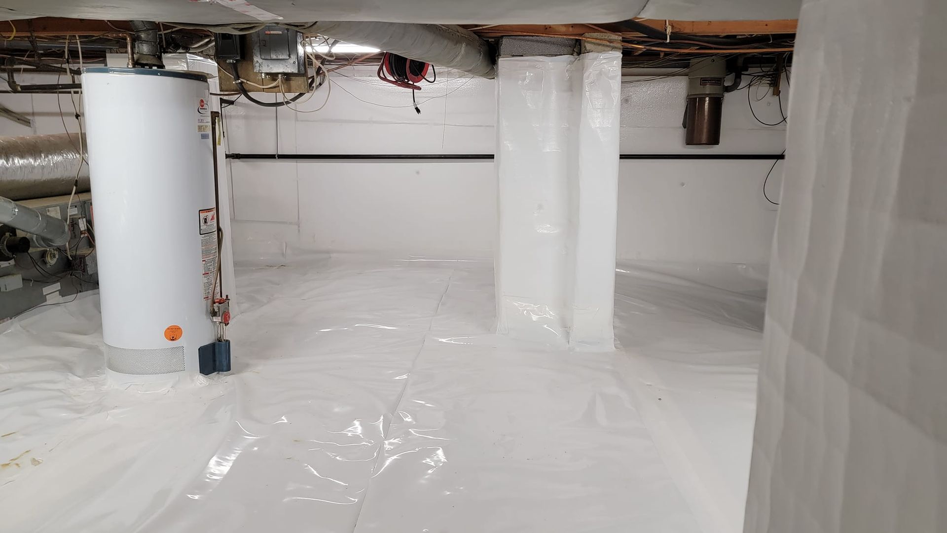 A basement with a water heater and pipes covered in plastic.
