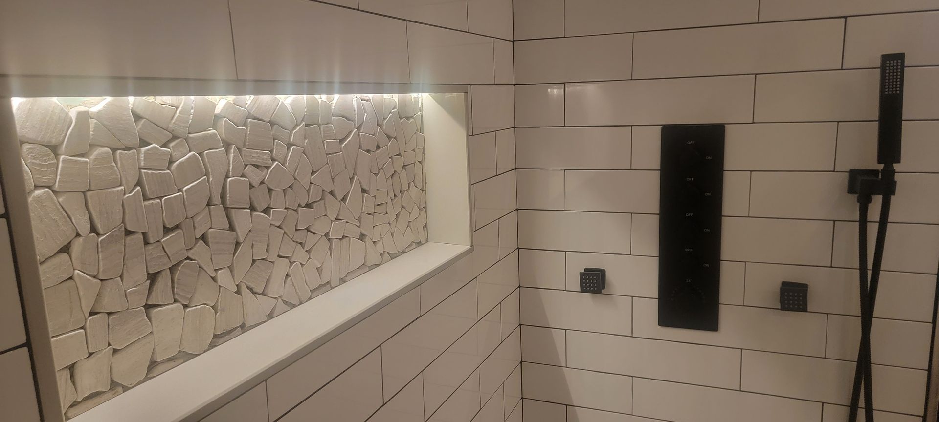 A bathroom with white tiles and a black shower head.