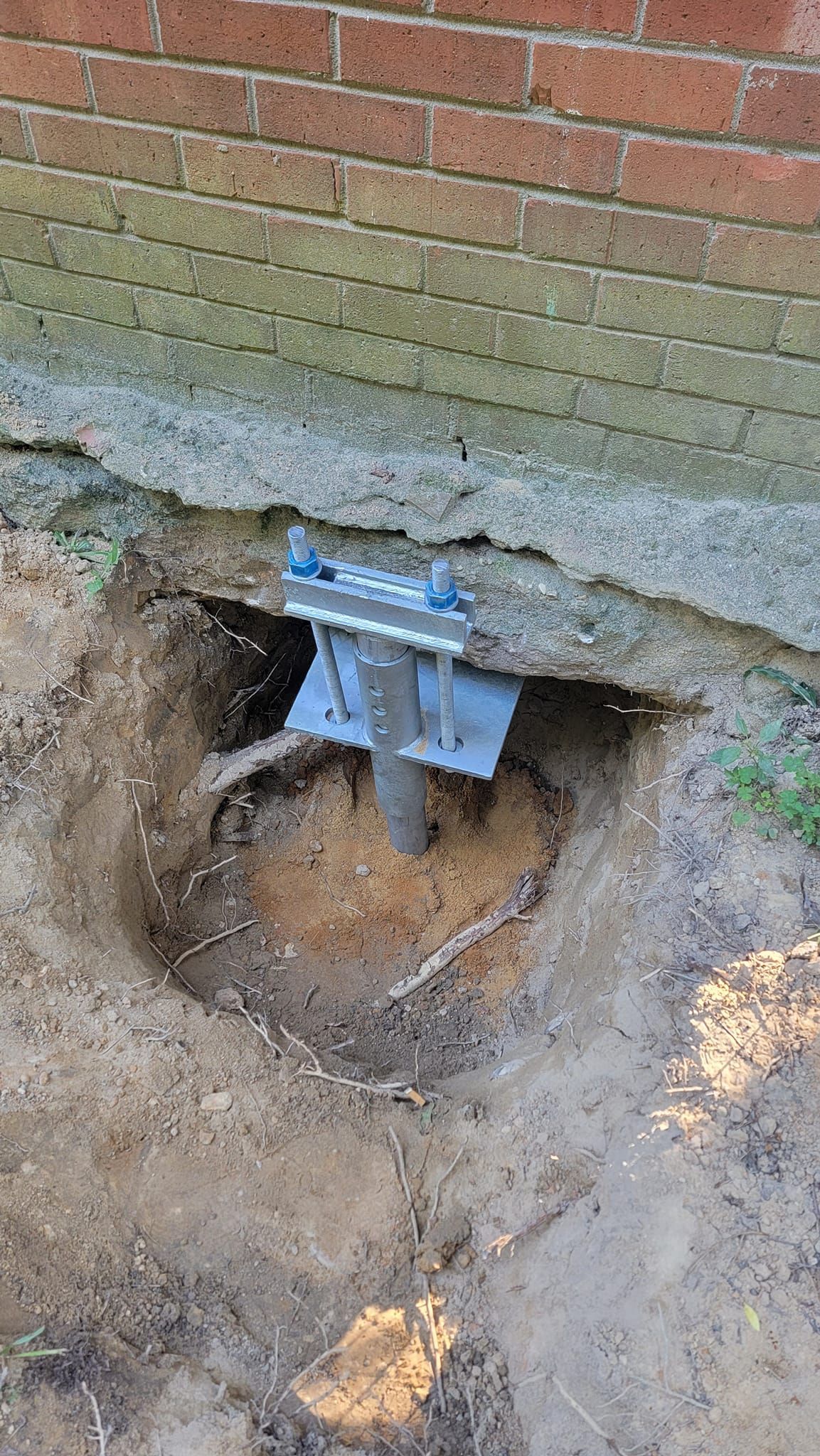 A metal anchor is sitting in the dirt next to a brick wall.