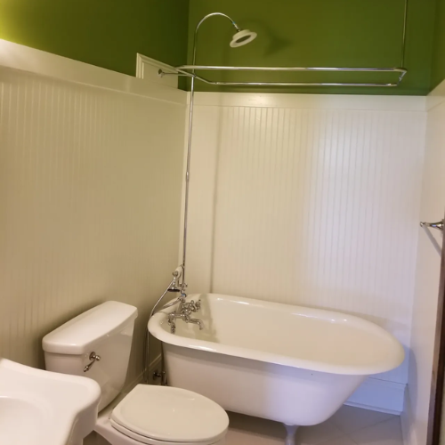 Bathroom with a white clawfoot tub, toilet, and beadboard walls. Green upper wall.