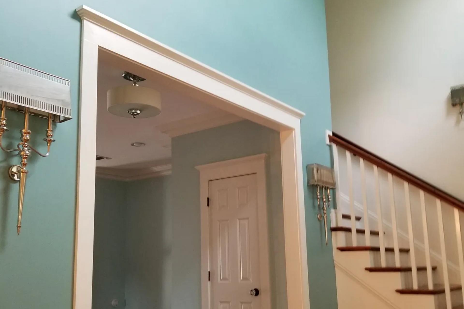 White-trimmed doorway and stairs with wood railing in a room with teal walls.