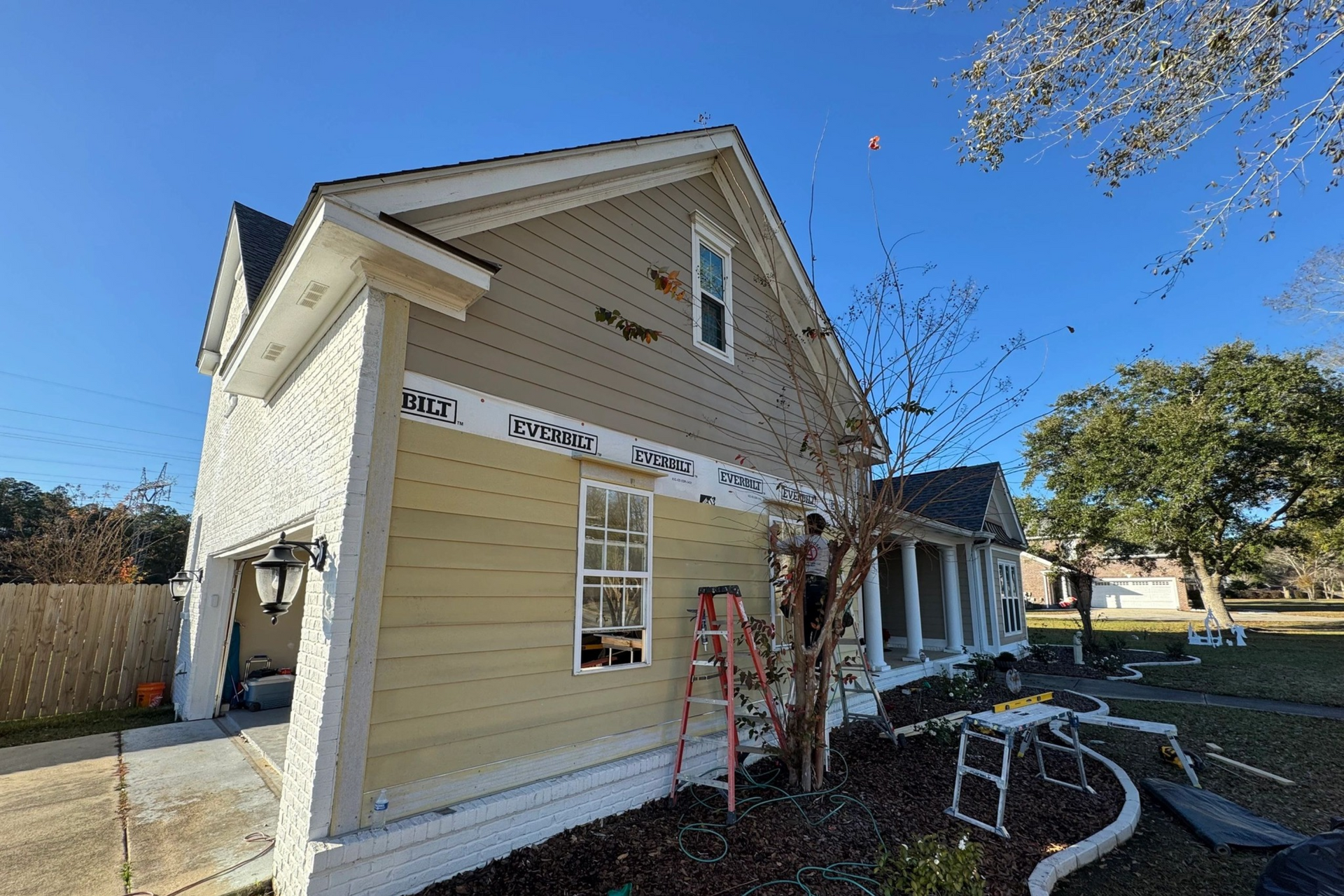 House exterior with siding partially installed, ladder, and blue sky.