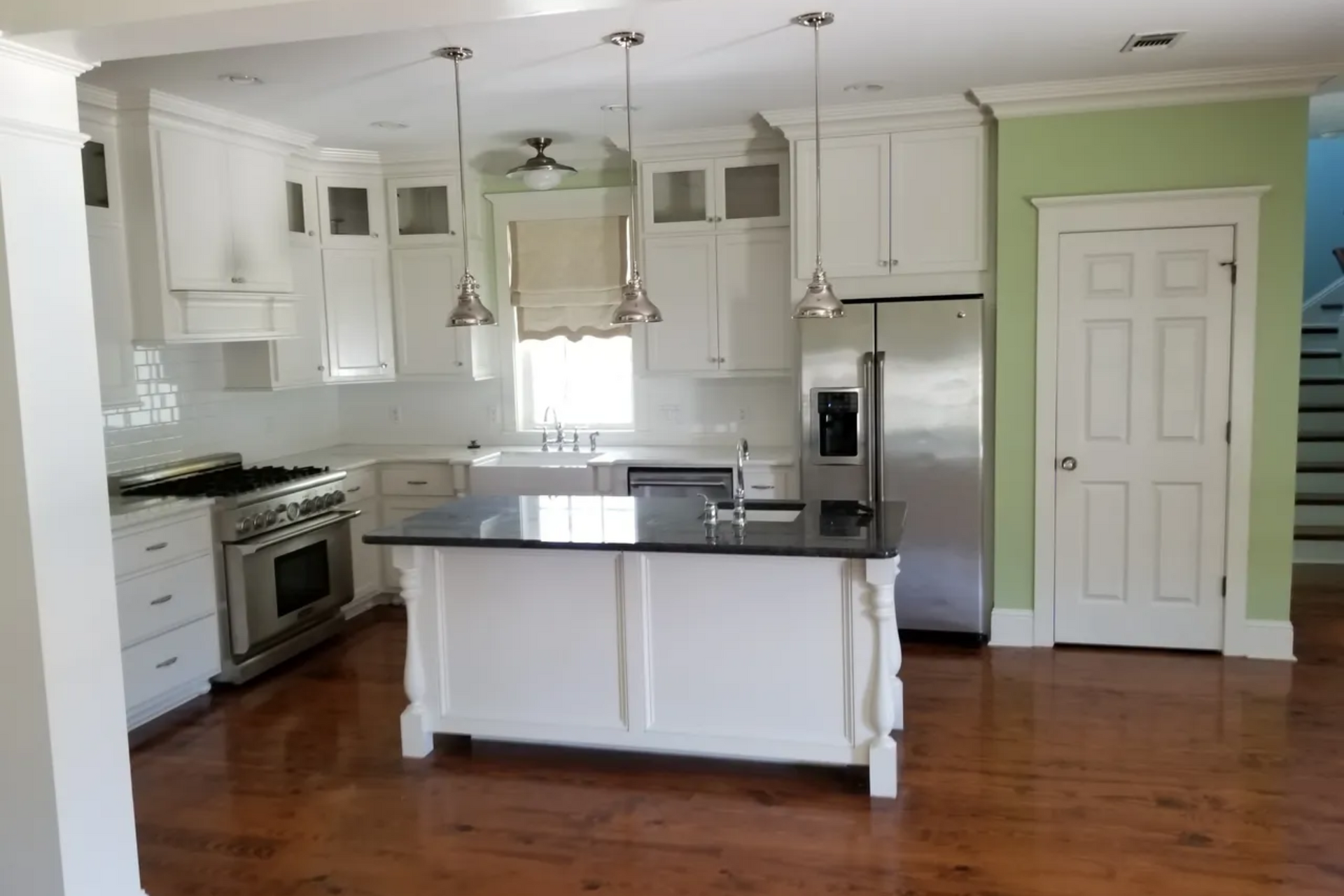 White kitchen with stainless steel appliances, island, and green wall.