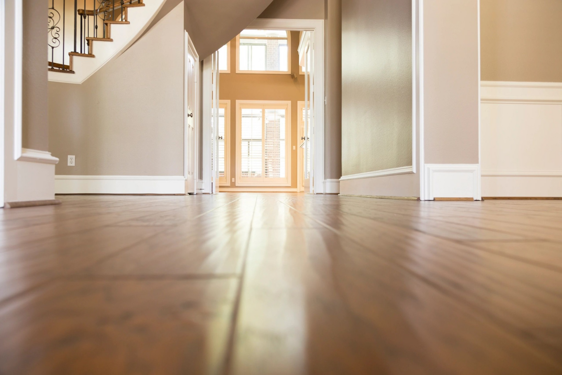 Wooden floor leading toward doorway and staircase in a house. Light reflects on the floor.