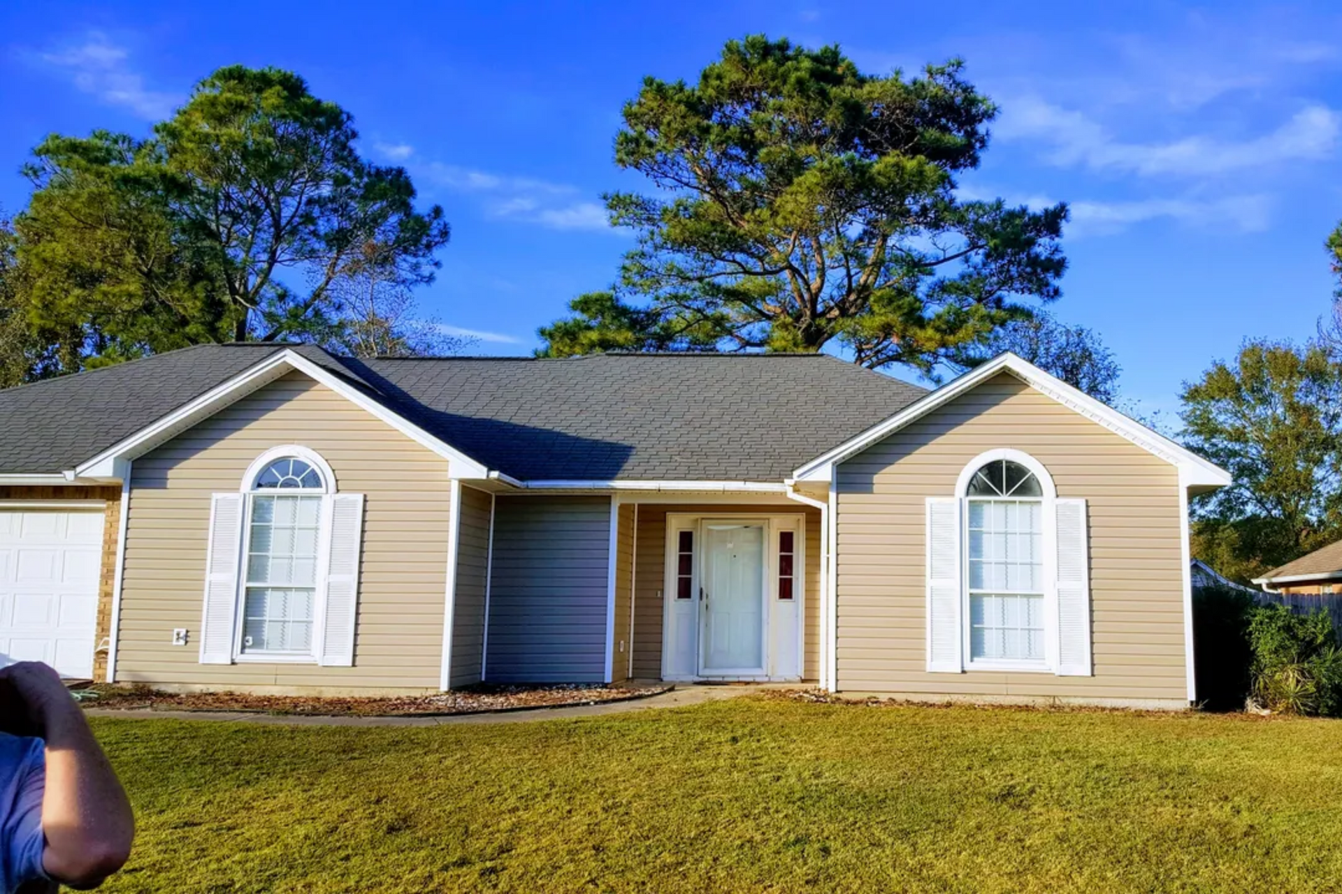 Beige house with white trim, arched windows, and green grass under a blue sky.