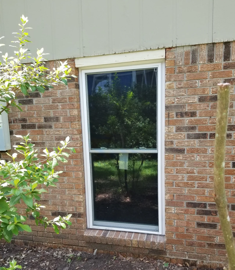 Tall window with white frame and dark tint in a brick wall, with a white awning.
