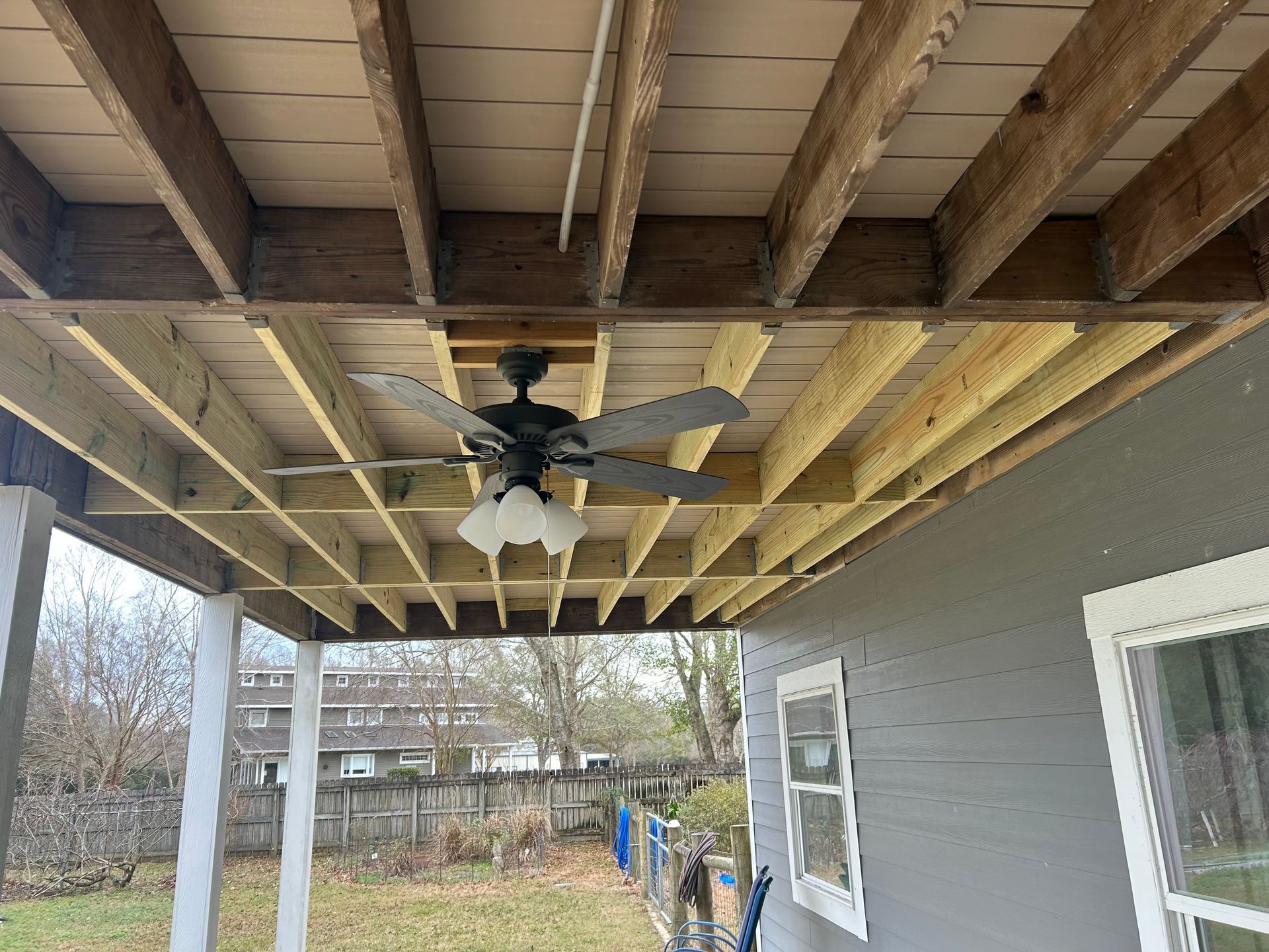 Ceiling of a porch with exposed beams, a ceiling fan, and painted white support posts.