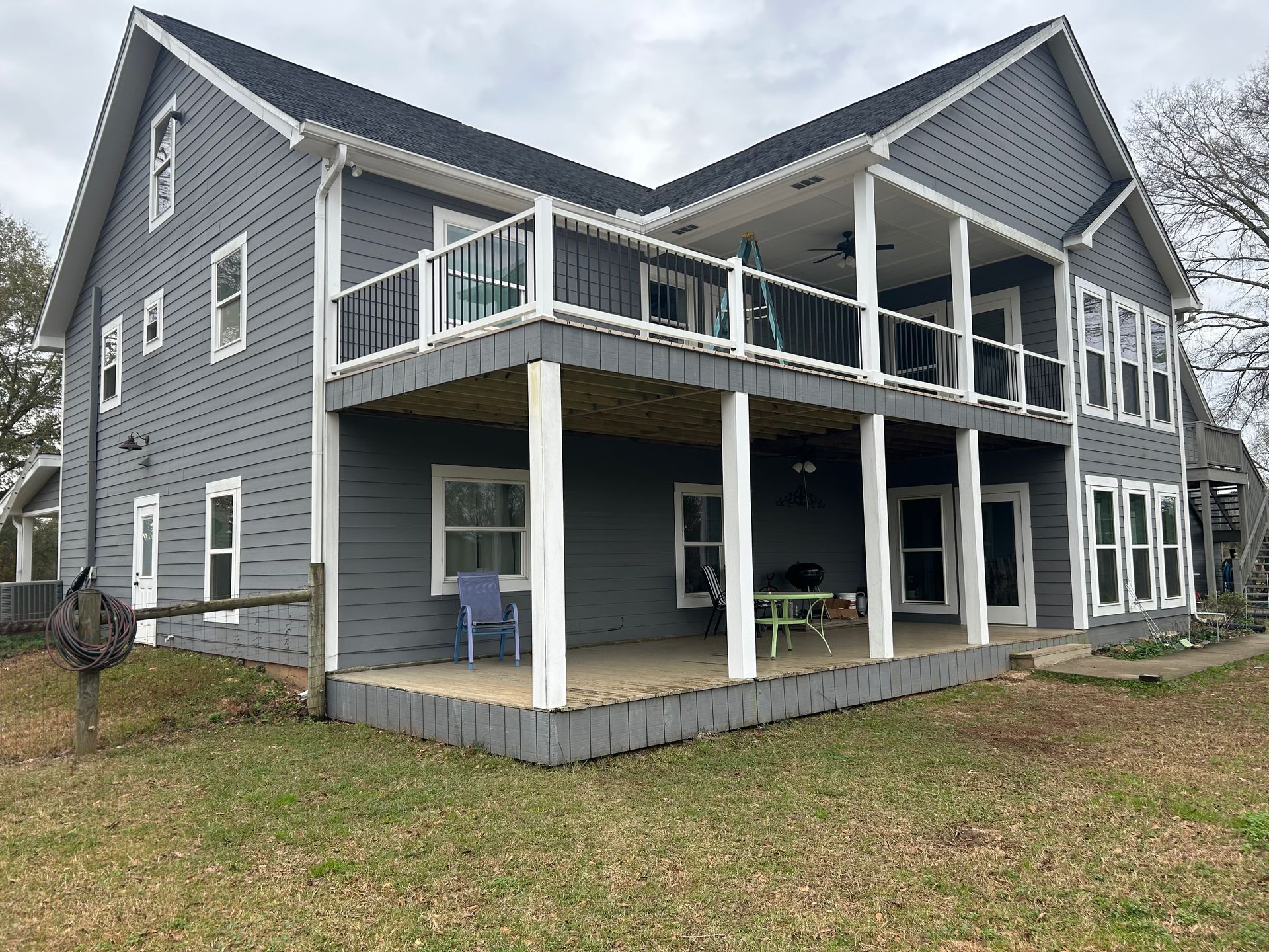 Two-story gray house with white trim, a large deck, and a yard of dry grass under an overcast sky.