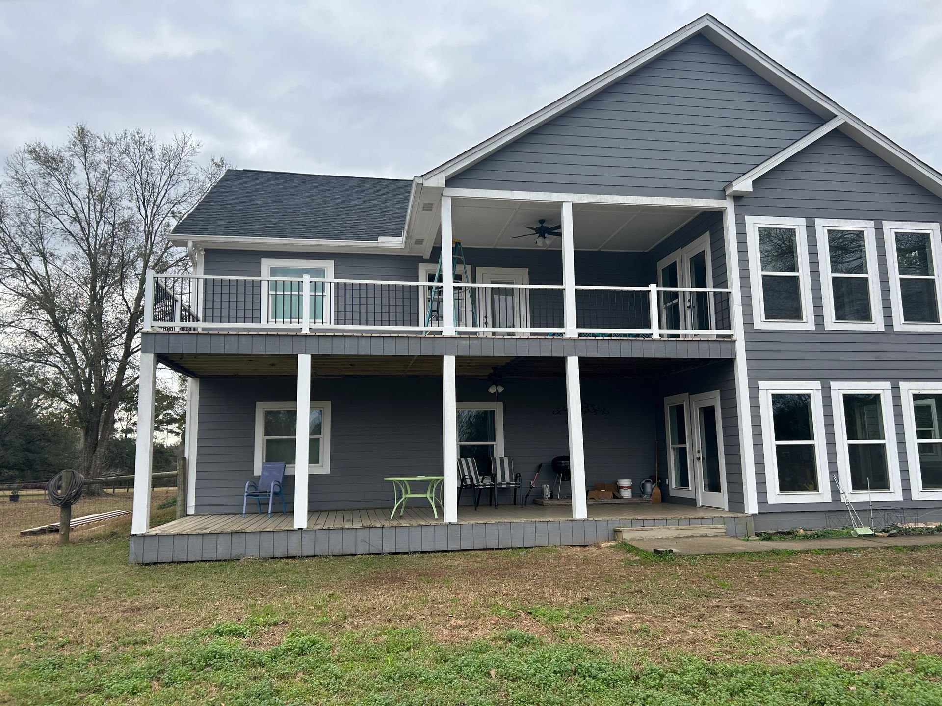 Two-story gray house with white trim and two-level deck on a cloudy day.