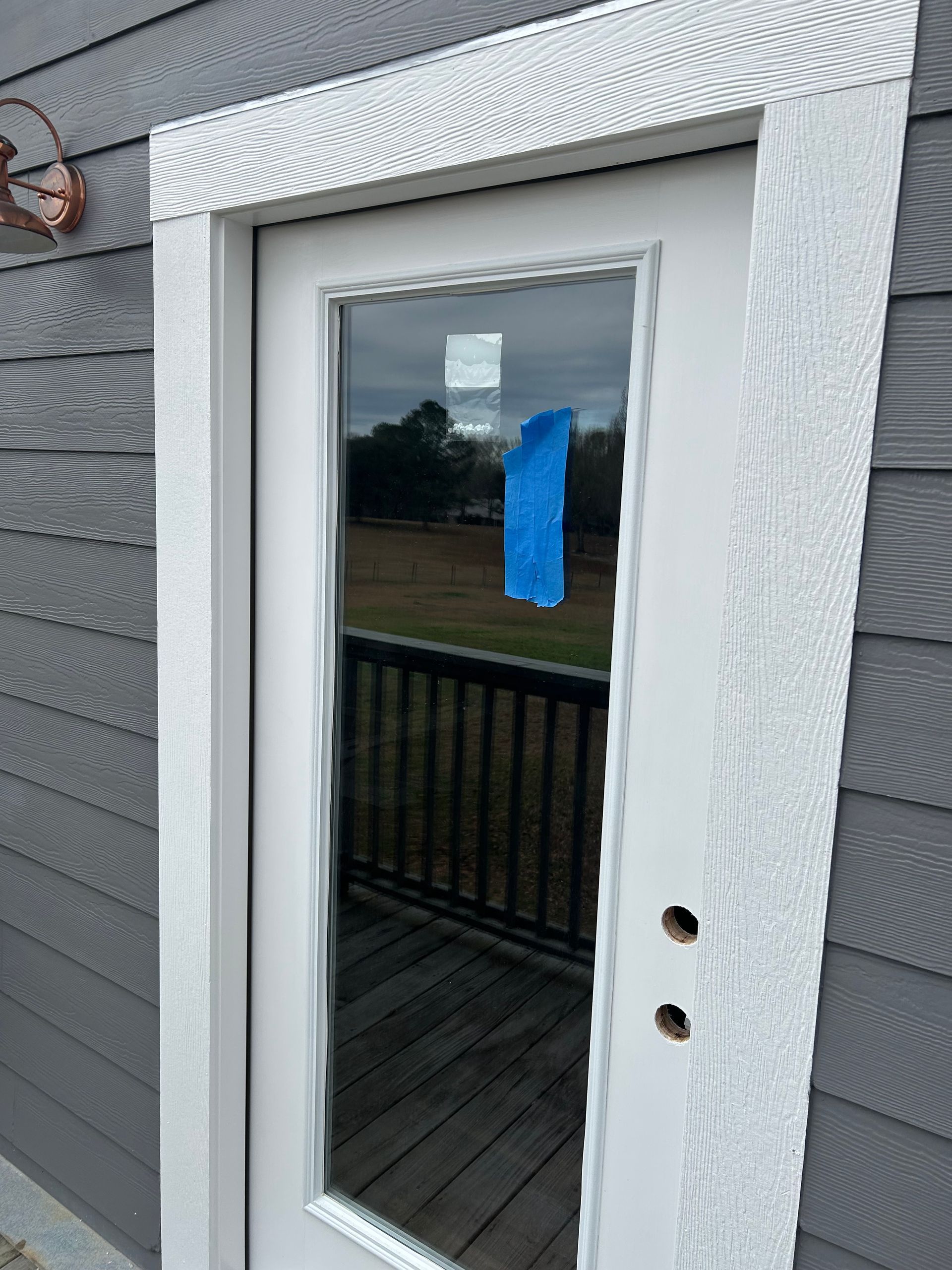 White door with glass pane, blue tape, white trim. Gray siding on the exterior of a building.