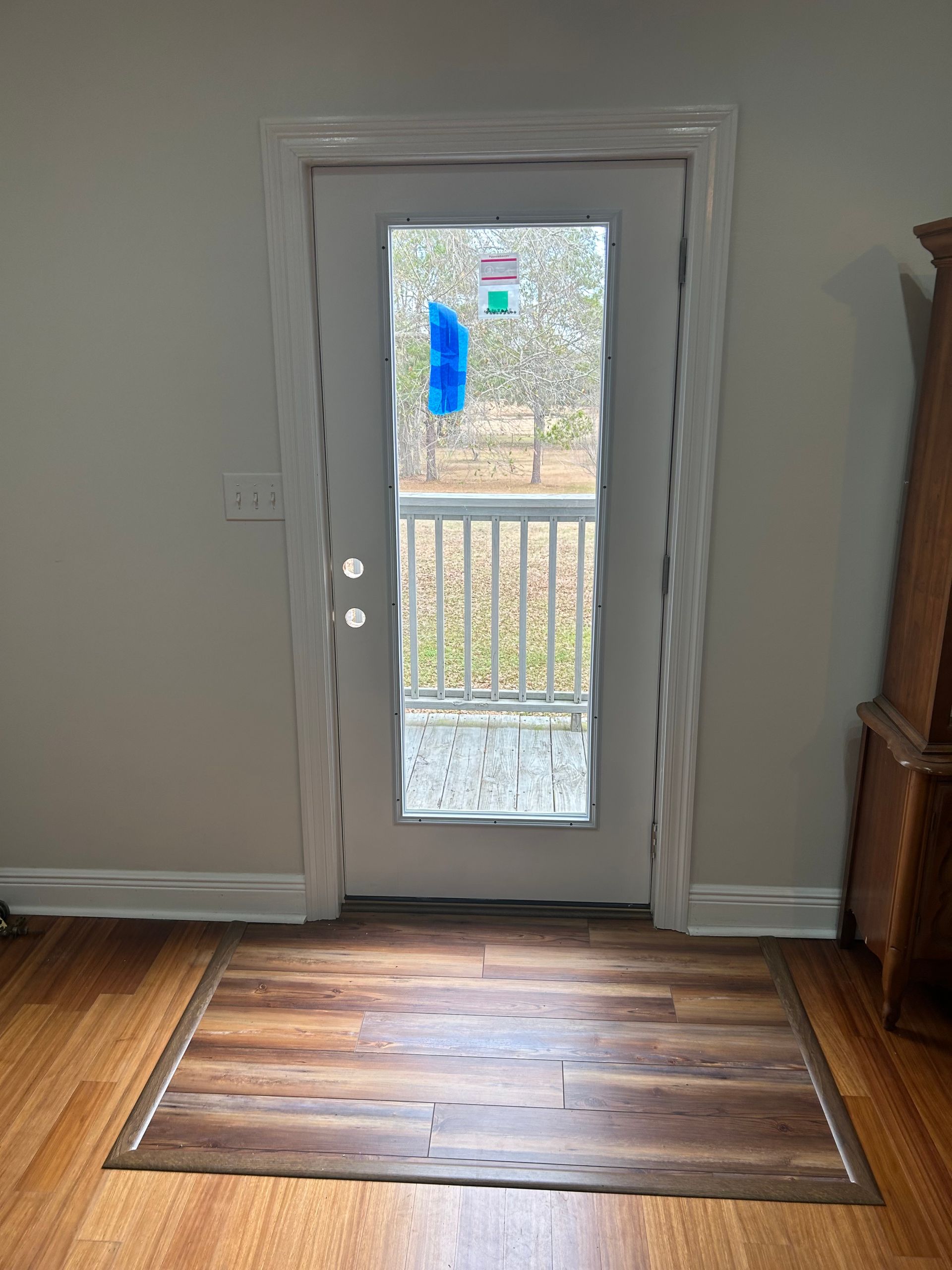 Interior view of a doorway leading to a deck. Door has a wavy glass panel. Wooden floor with mat.