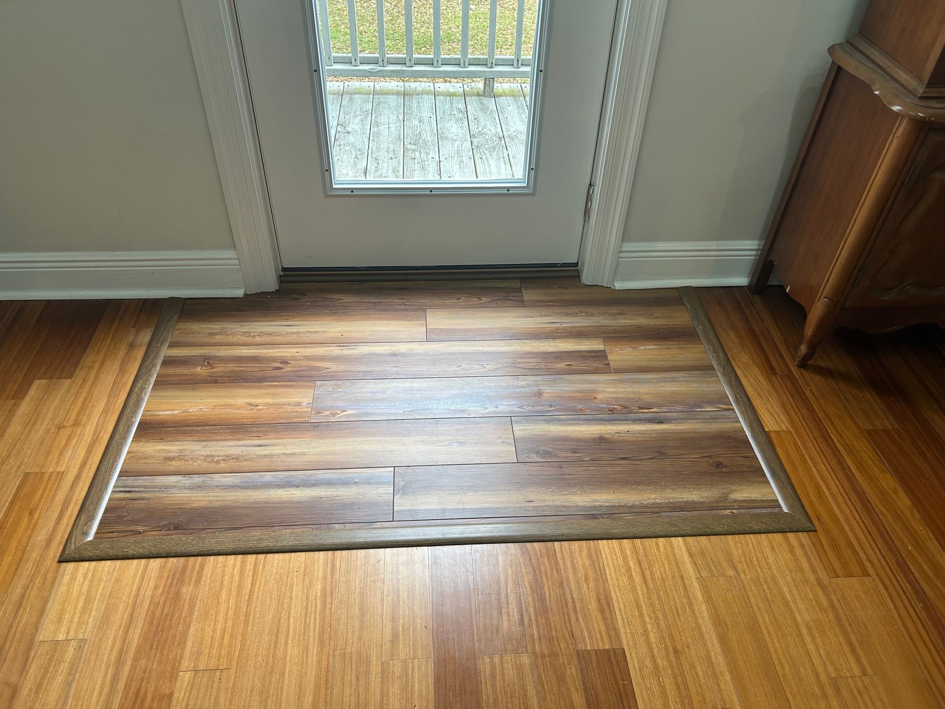 Wooden flooring with a rectangular insert and doorway in the background.