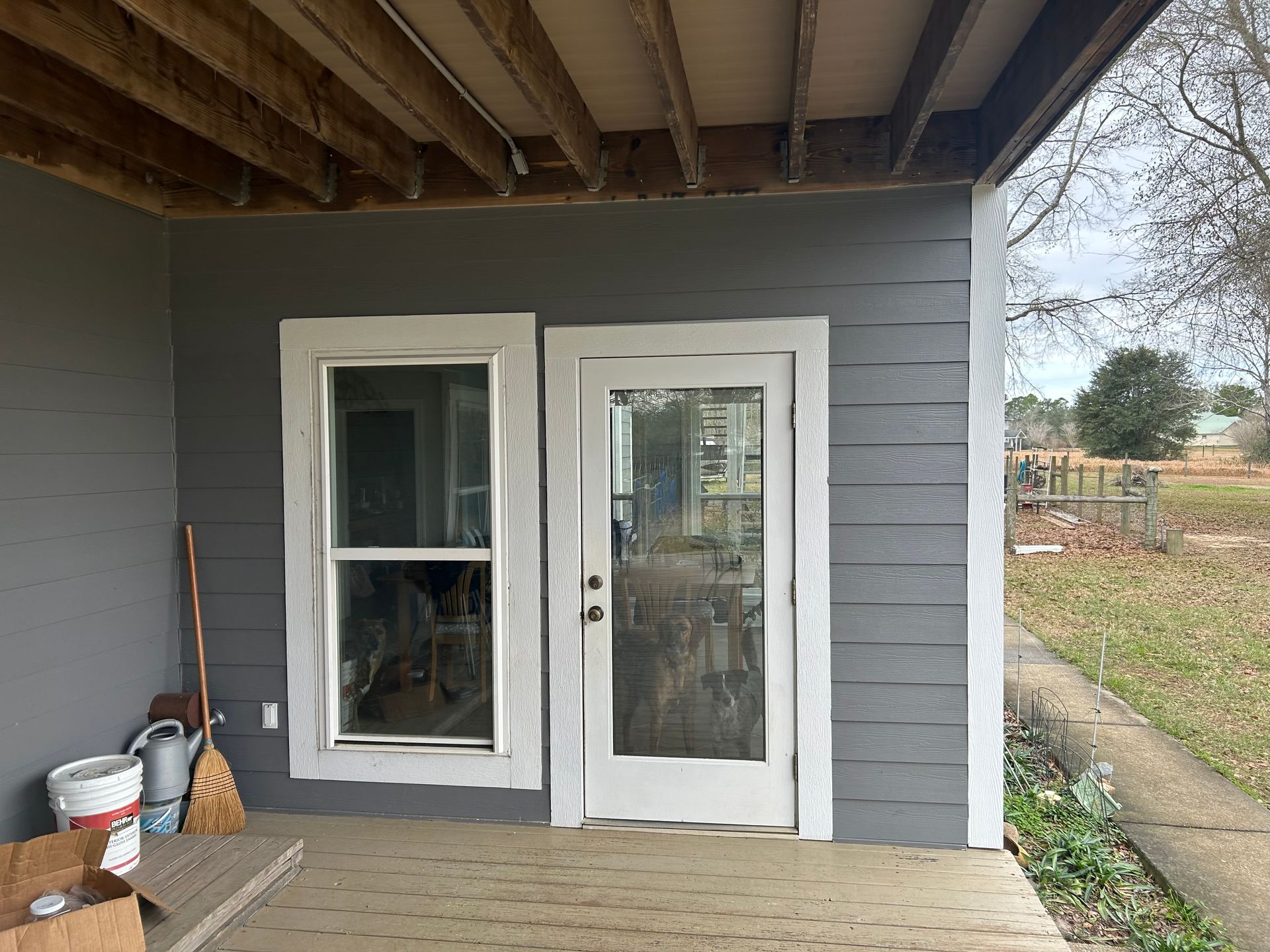 Window and glass-paned door on a covered porch, white frames against gray siding.