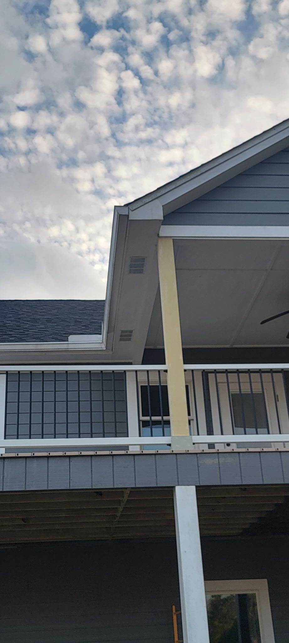 Exterior view of a house with a deck and blue siding. Cloudy sky visible.