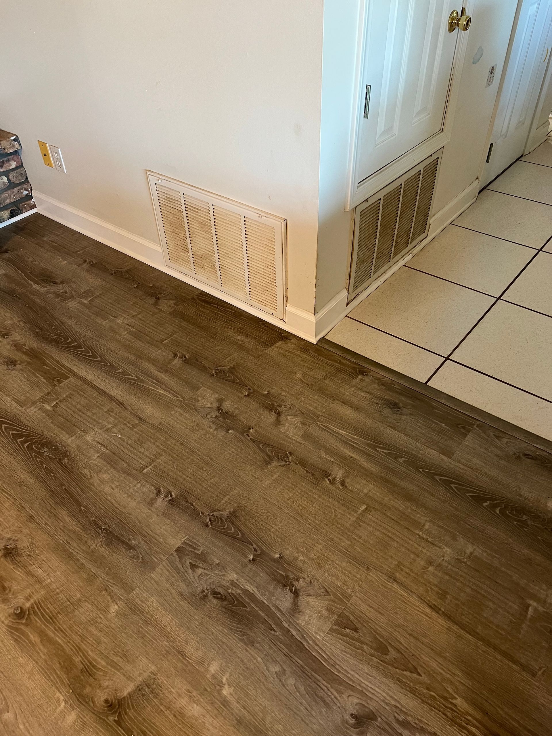 Two dirty air vents on white walls, next to wood and tiled floors.