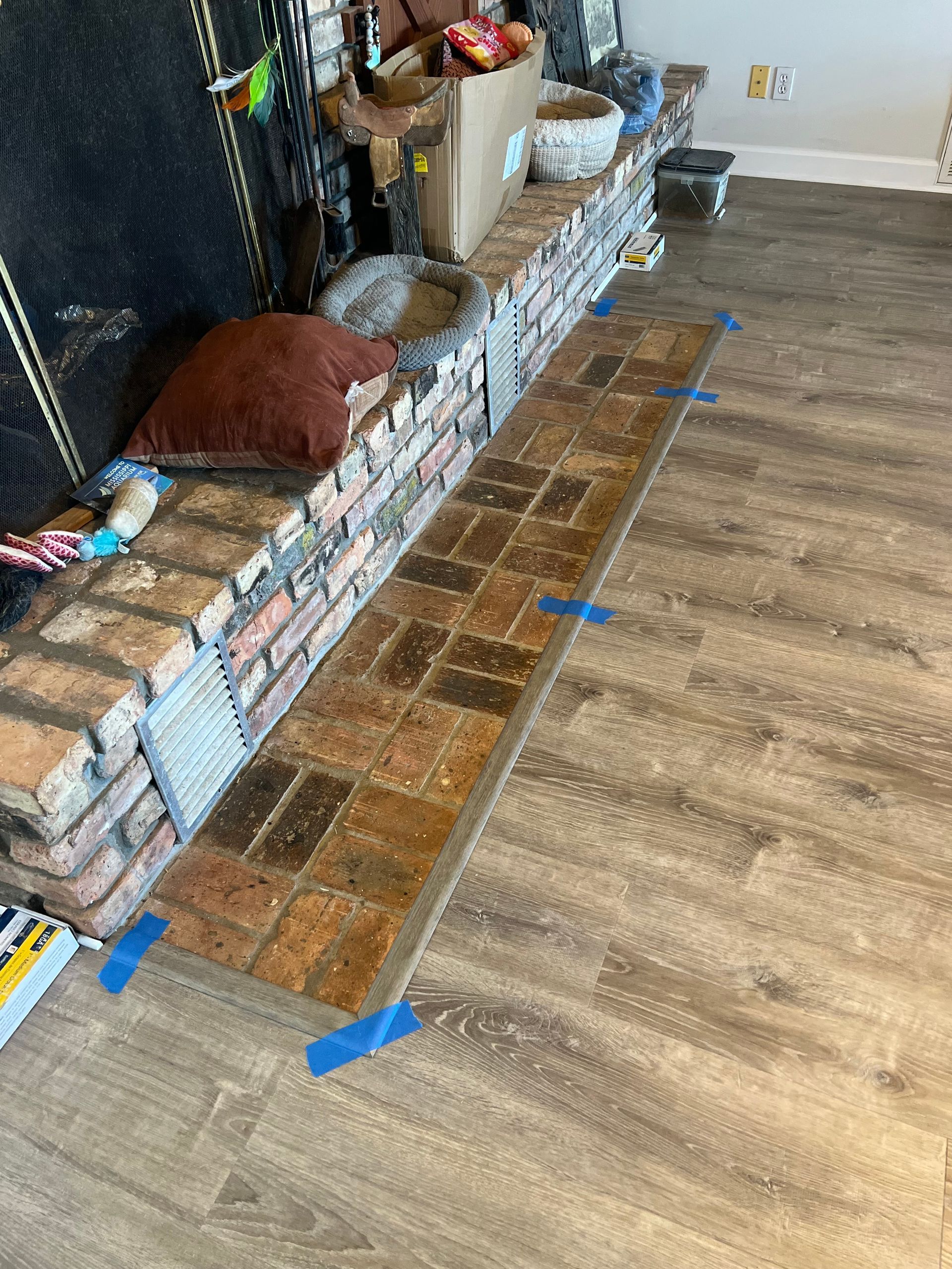 Brick hearth extension on wood-look floor, taped, near a brick fireplace.