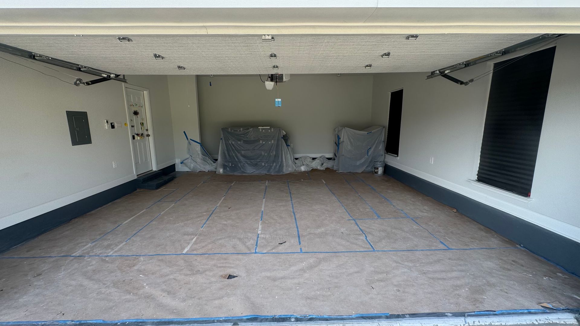 Empty garage interior with floor marked, two covered objects, and a camera.