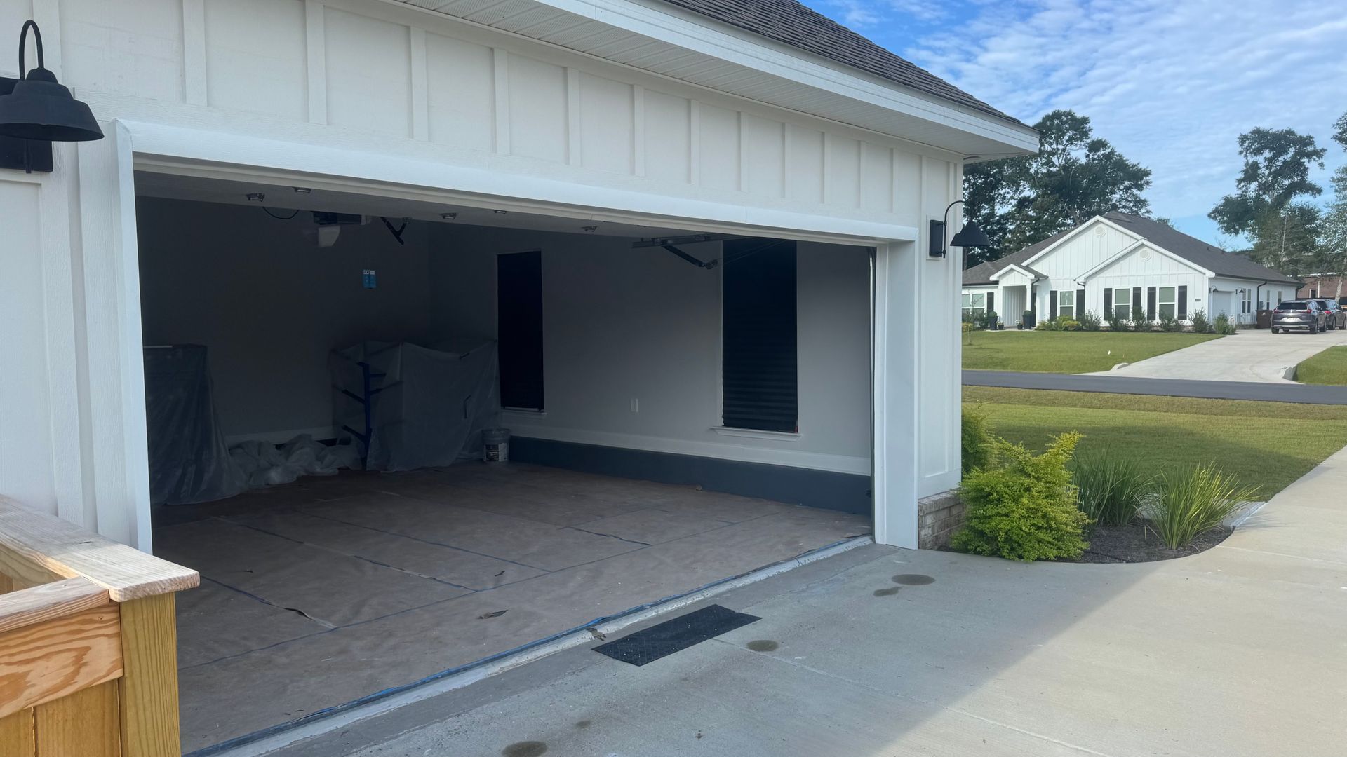 Open garage with interior visible; white exterior, black accents; house and lawn in background.