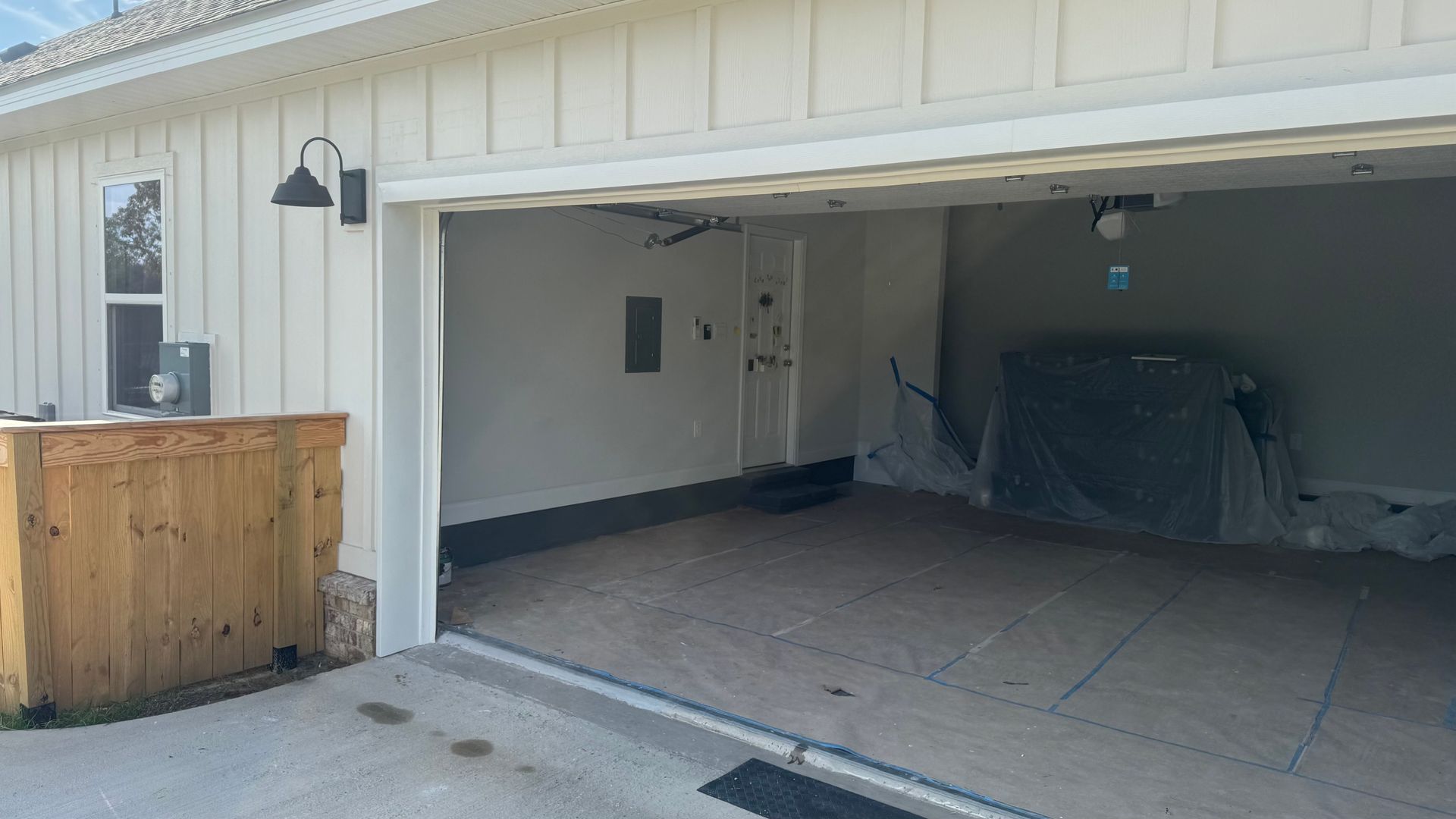 Exterior view of an open garage with white siding and a wooden bar area to the left.