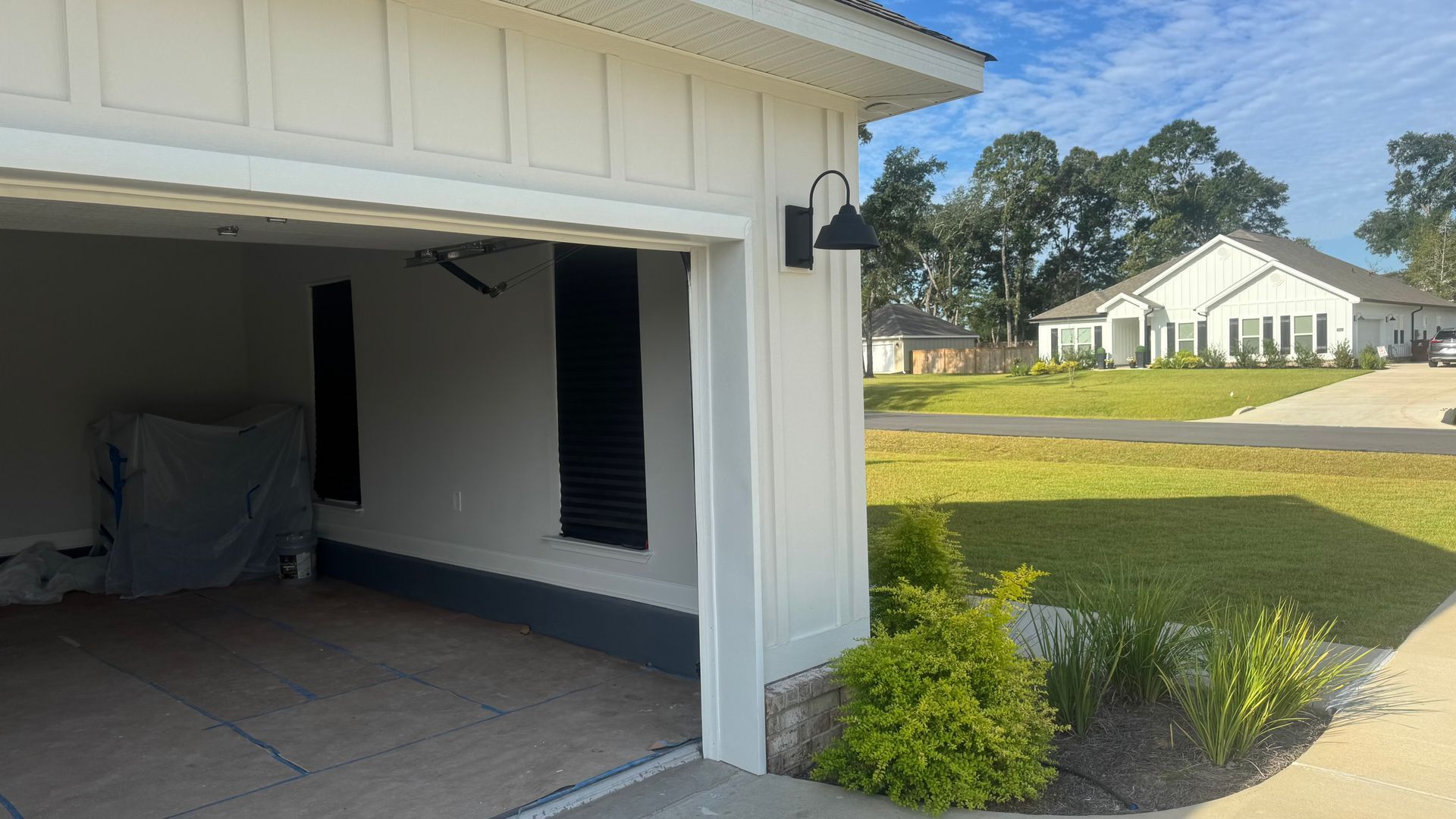 Exterior of a white house with an open garage. A black light fixture hangs above. Landscaping in front.