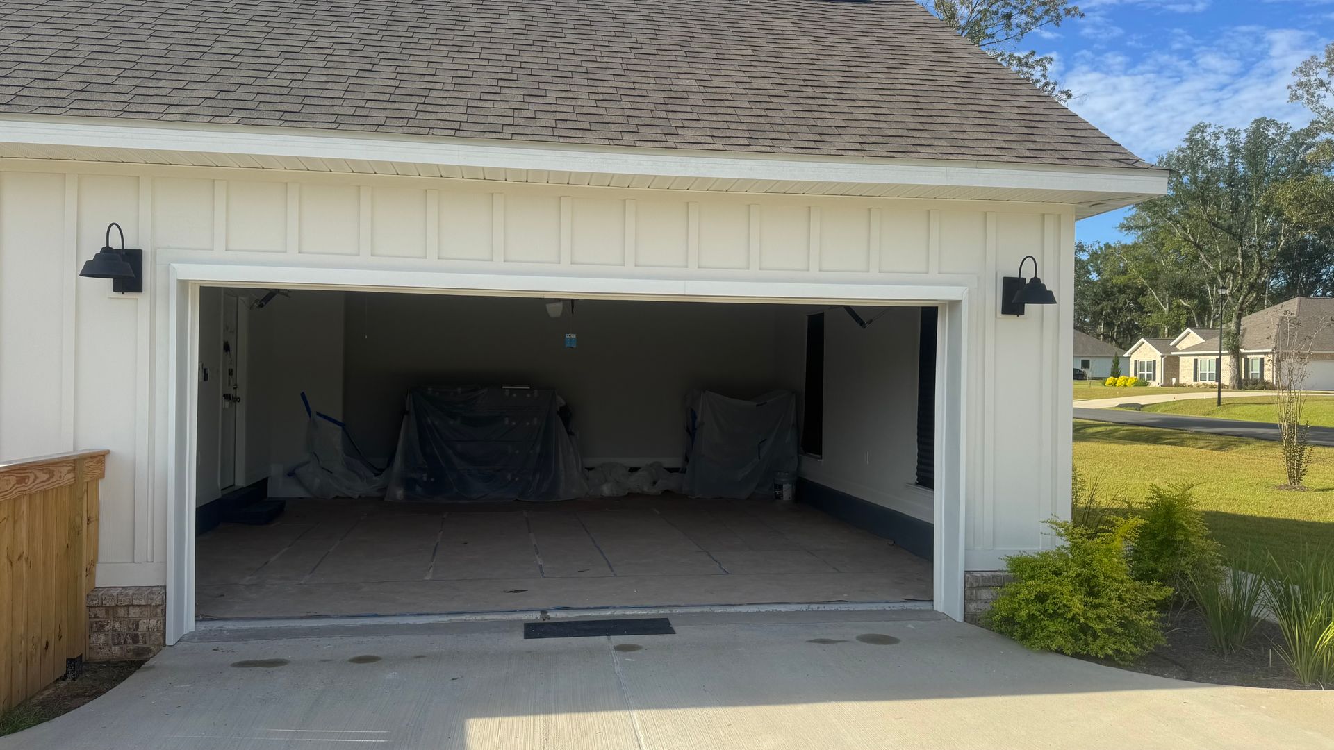 Garage with open door, white exterior, concrete driveway, and black sconces.