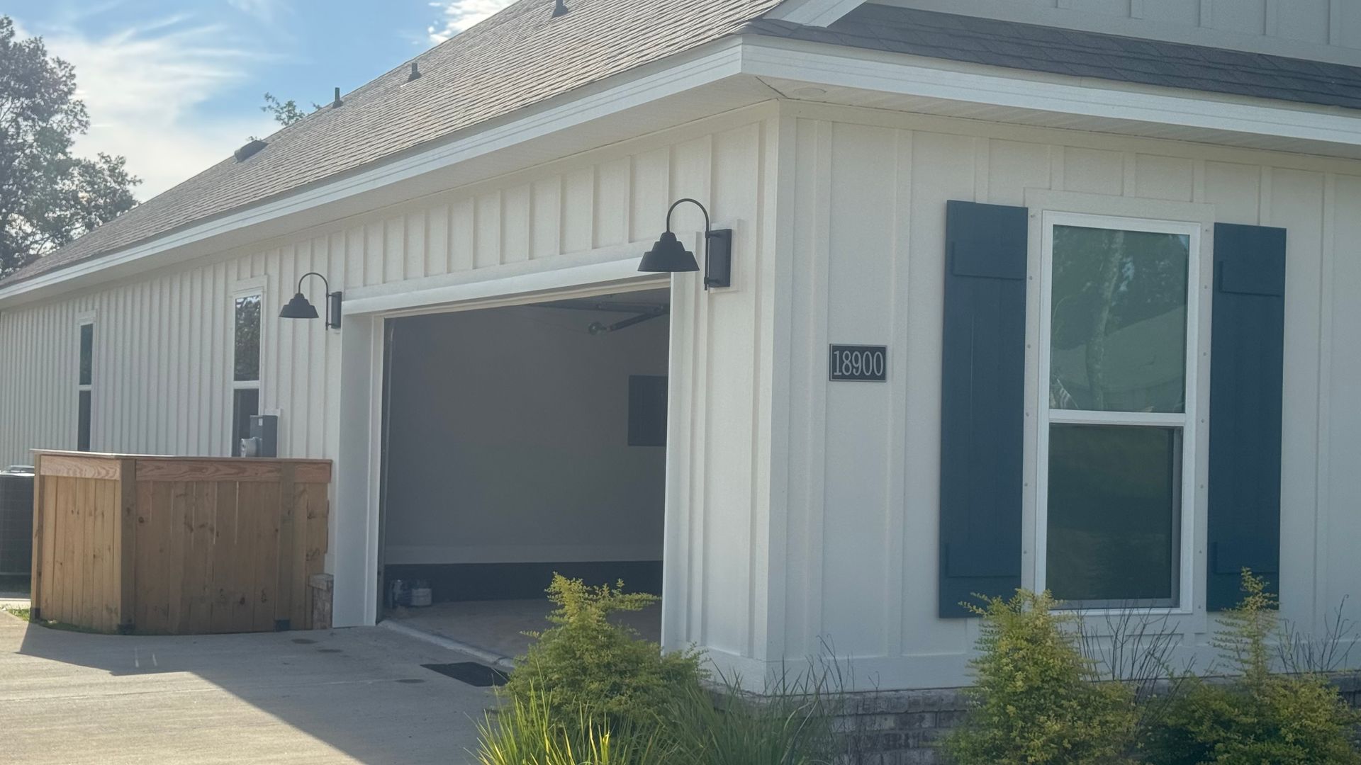 White house exterior with open garage, blue shutters, black sconces, and address number.