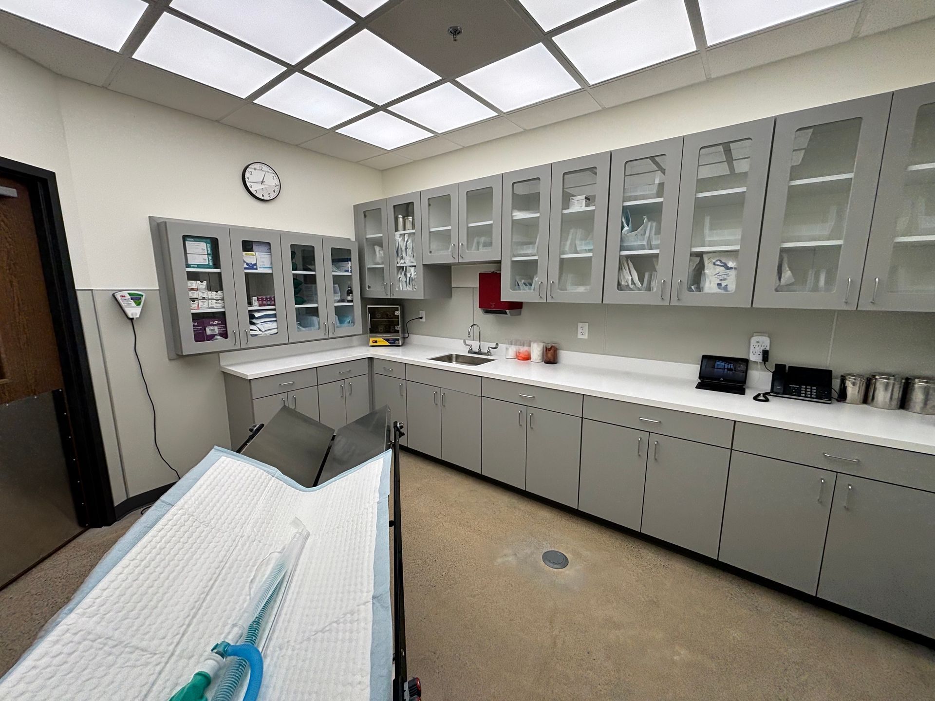 A clean, modern medical examination room featuring gray cabinetry, a sink, and a paper-covered exam table.
