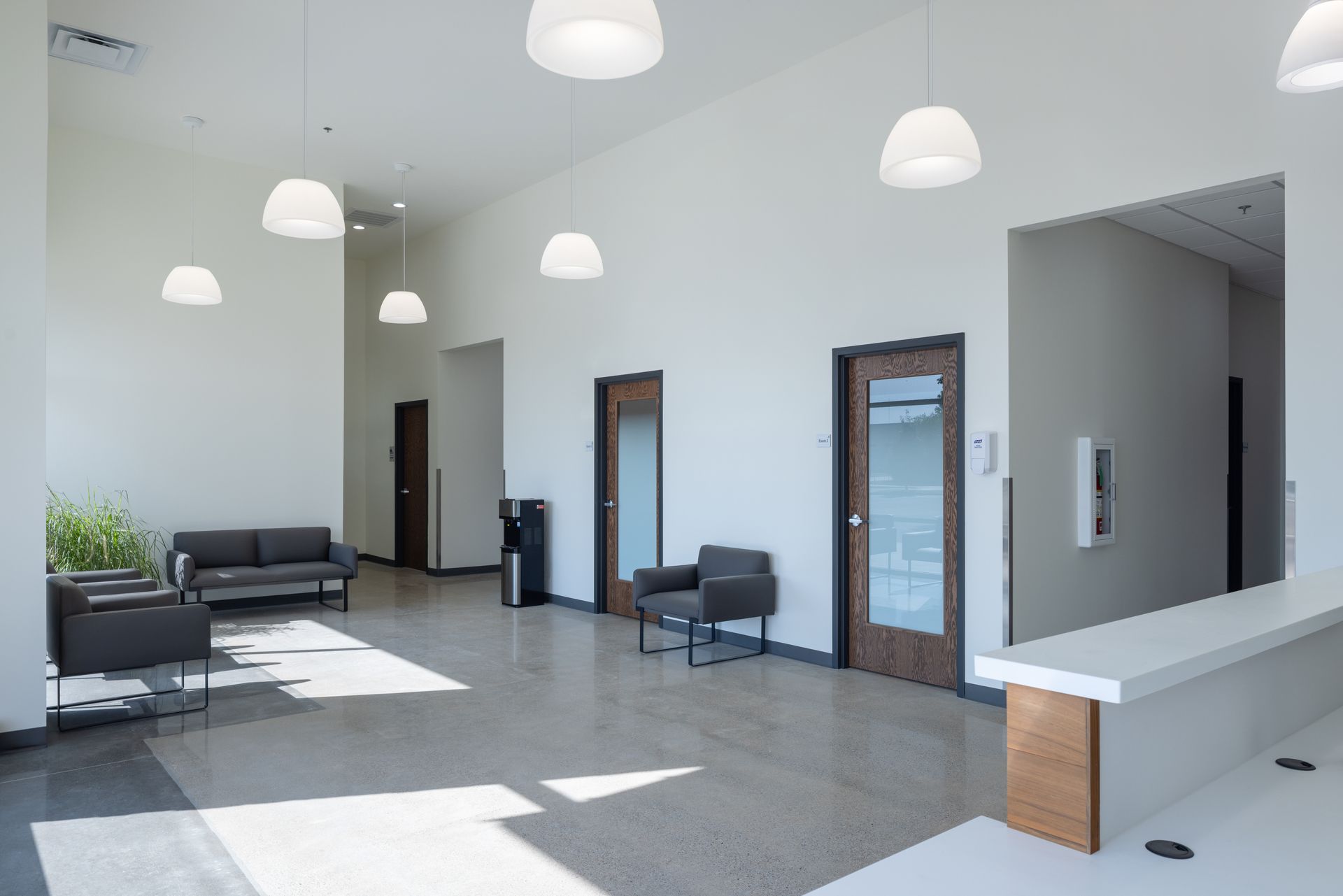A modern veterinary clinical workspace with exam tables, medical shelving, stainless steel kennels, and office chairs.