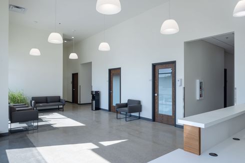 A modern veterinary clinical workspace with exam tables, medical shelving, stainless steel kennels, and office chairs.