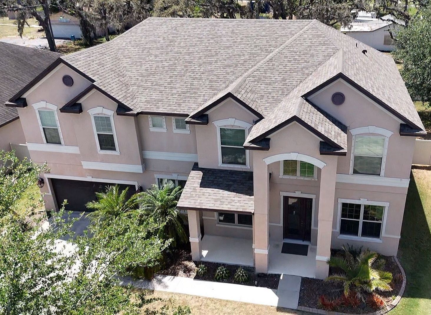 Two-story stucco house with a gray roof and black trim. Lush landscaping in front.