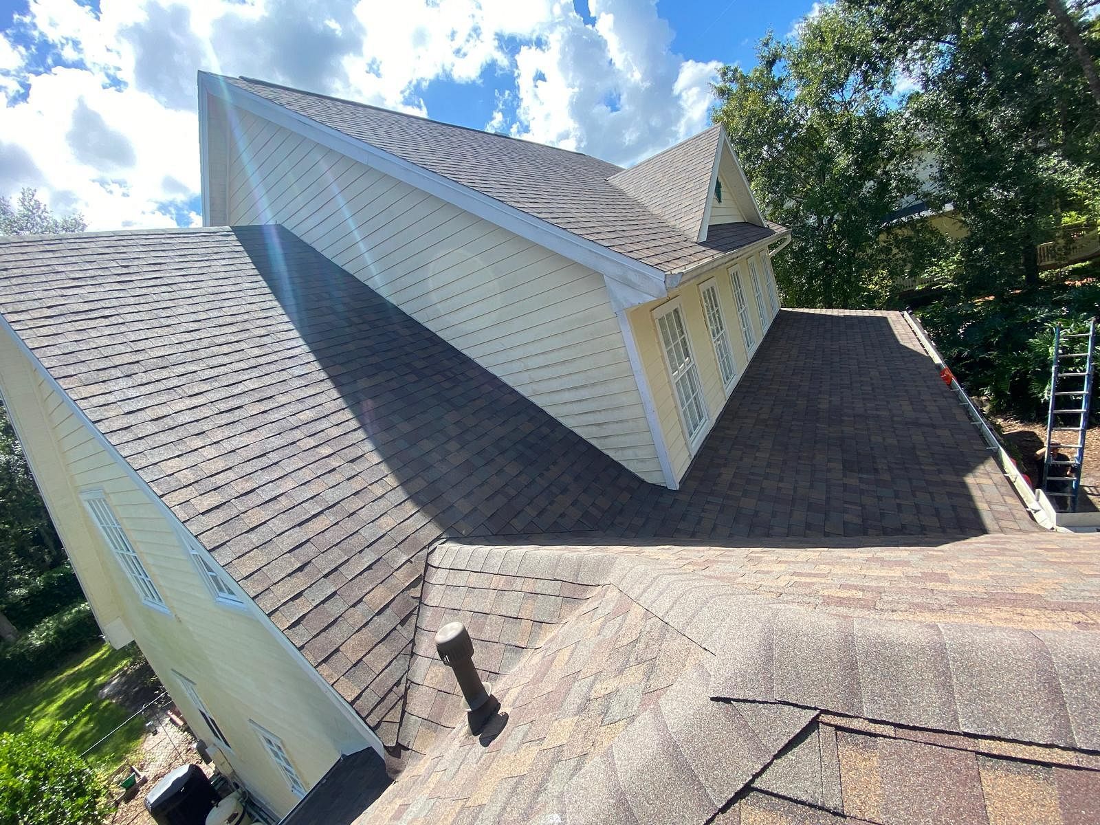 Brown shingled roofs of a two-story house against a blue, cloudy sky.