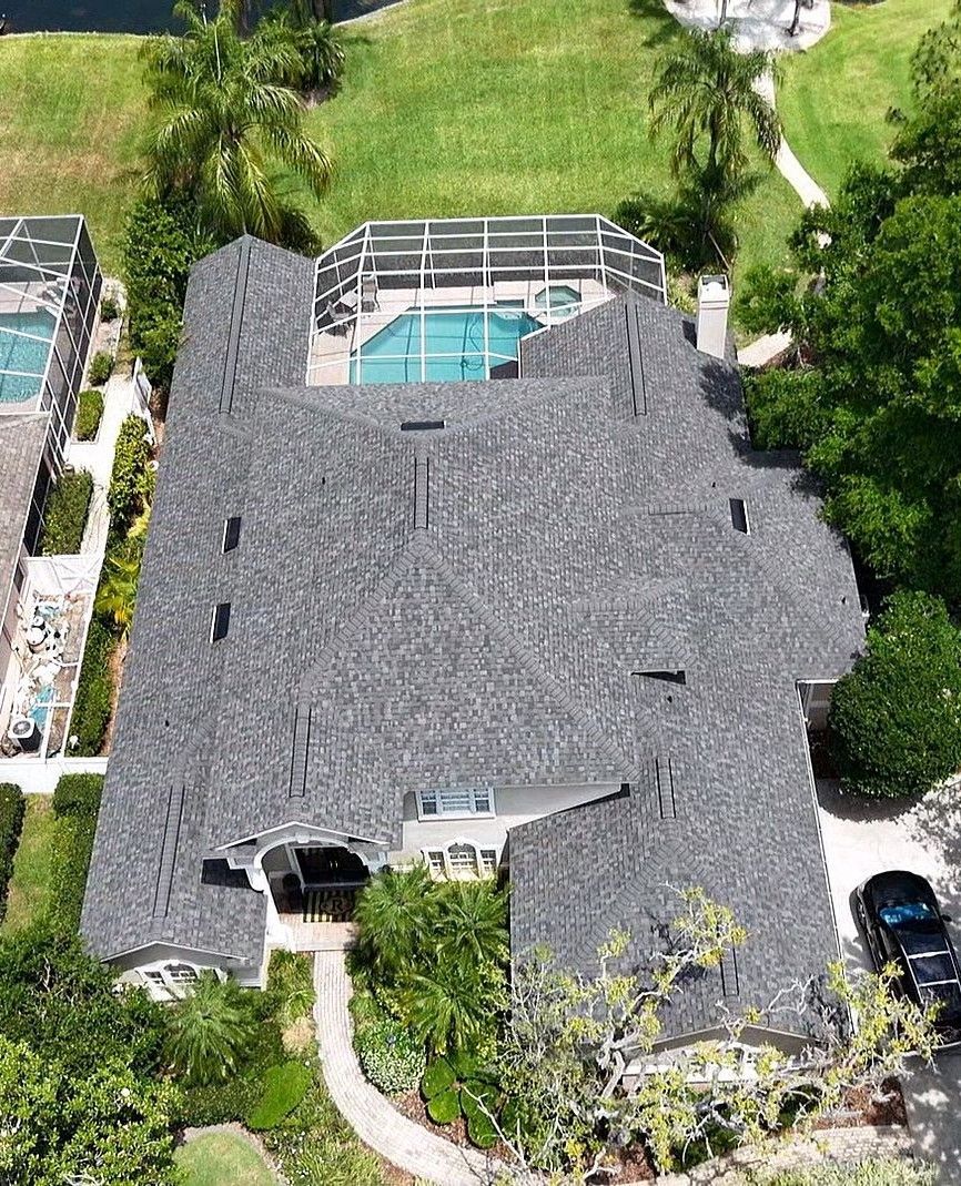 Aerial view of a home with a thatched roof, pool, and green surroundings.