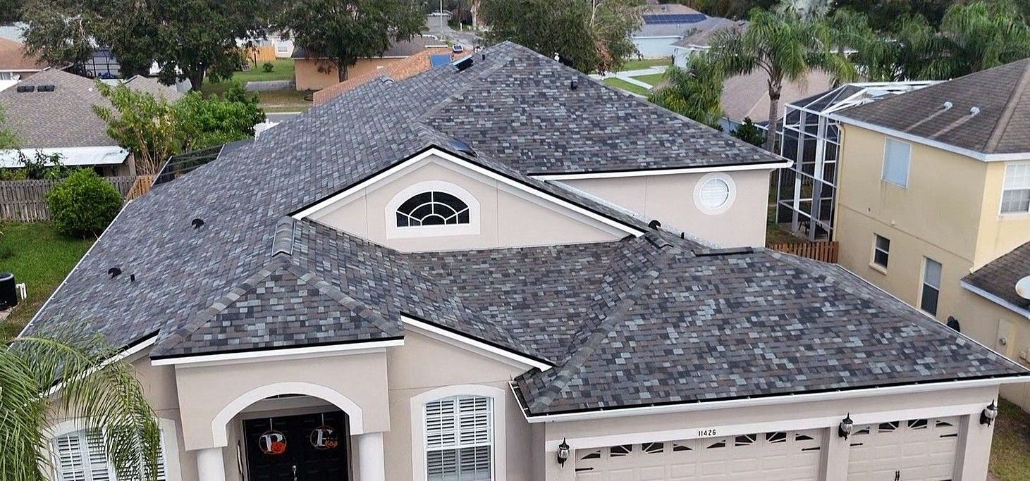 Overhead view of a two-story beige house with a dark gray roof. Other houses and trees surround.