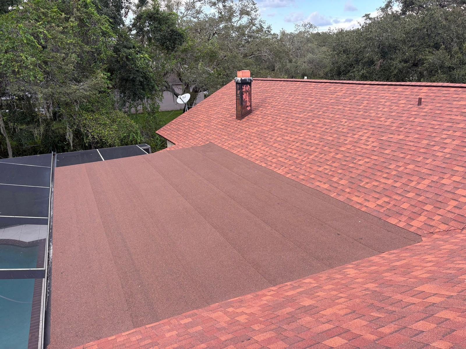 Red asphalt shingle roof with a flat, dark roof section and a chimney, viewed from above.